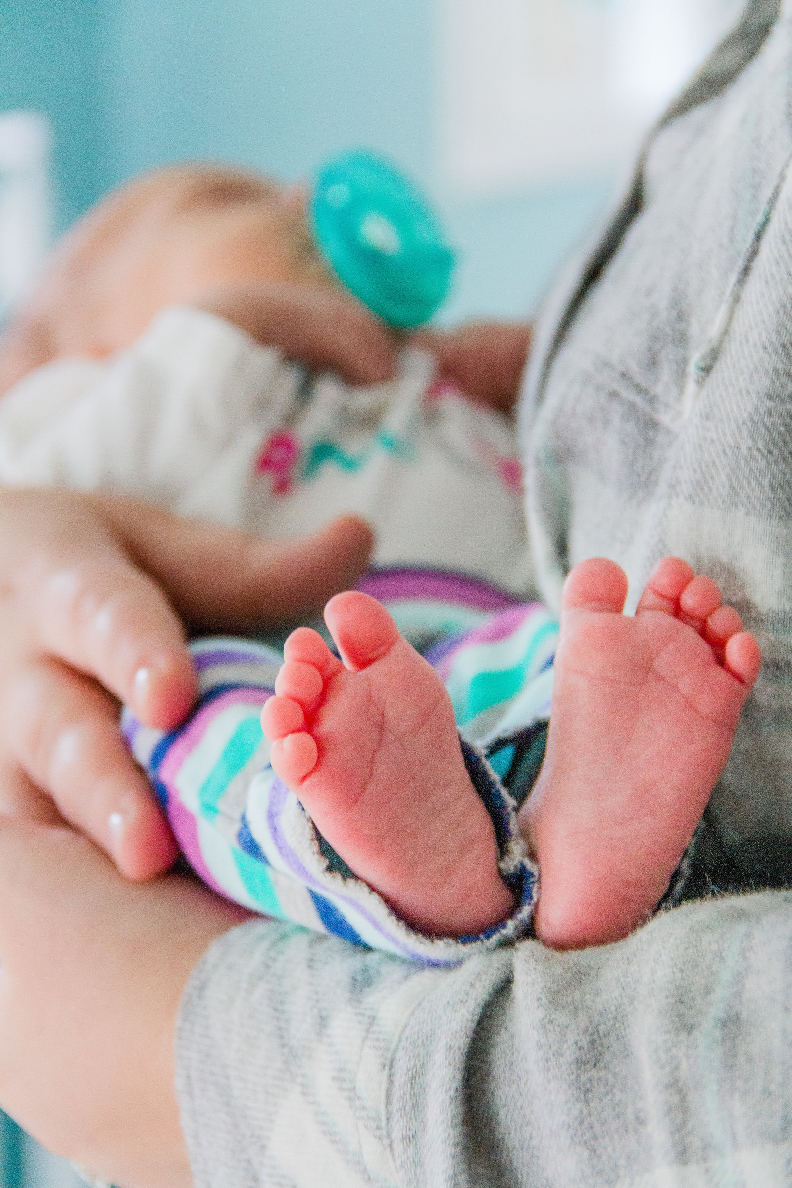 Newborn baby toes face the camera while the infant is held in her moms arms
