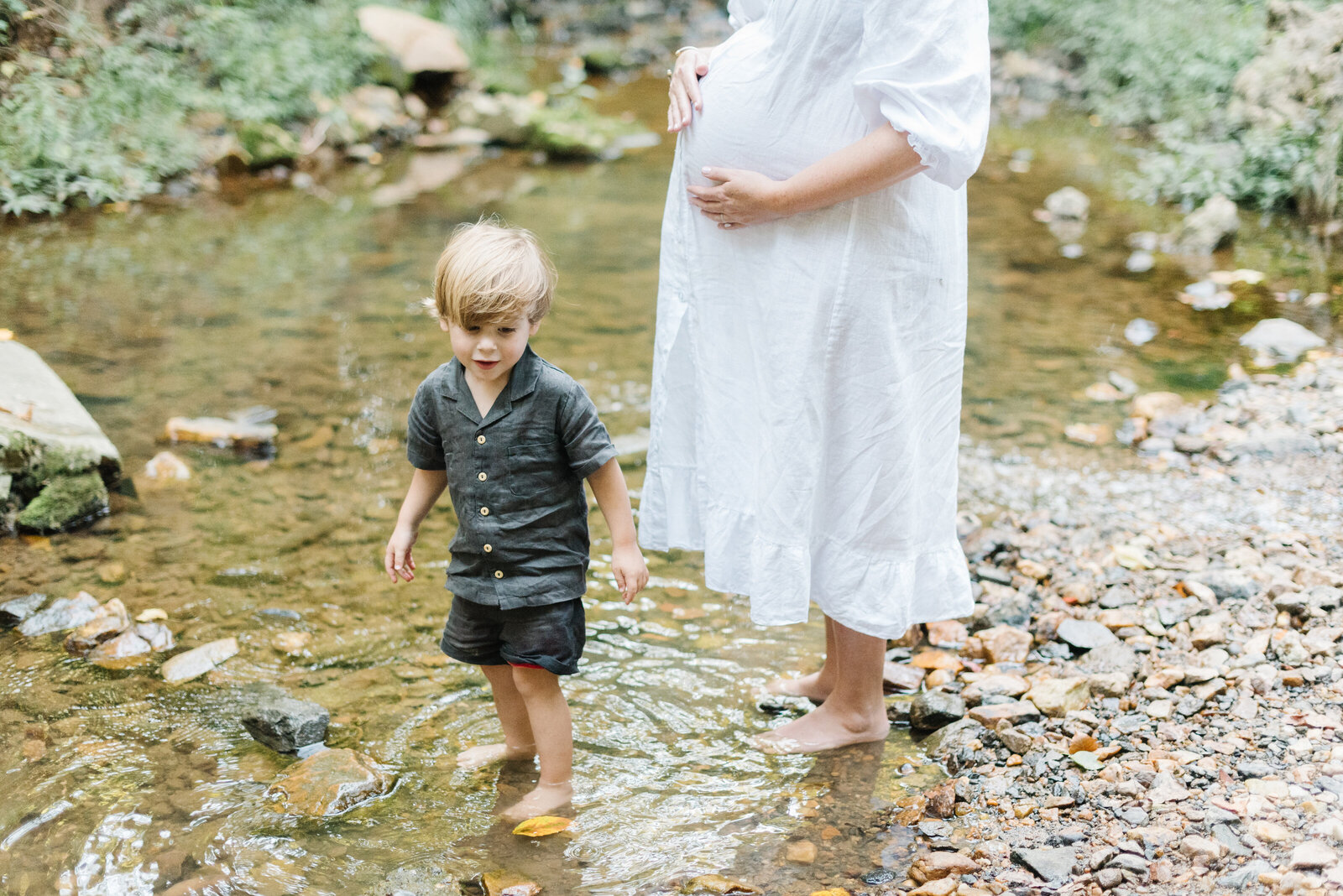 Blond child standing in creek with pregnant mother standing nearby with hand on belly - Washington DC Maternity Photographer