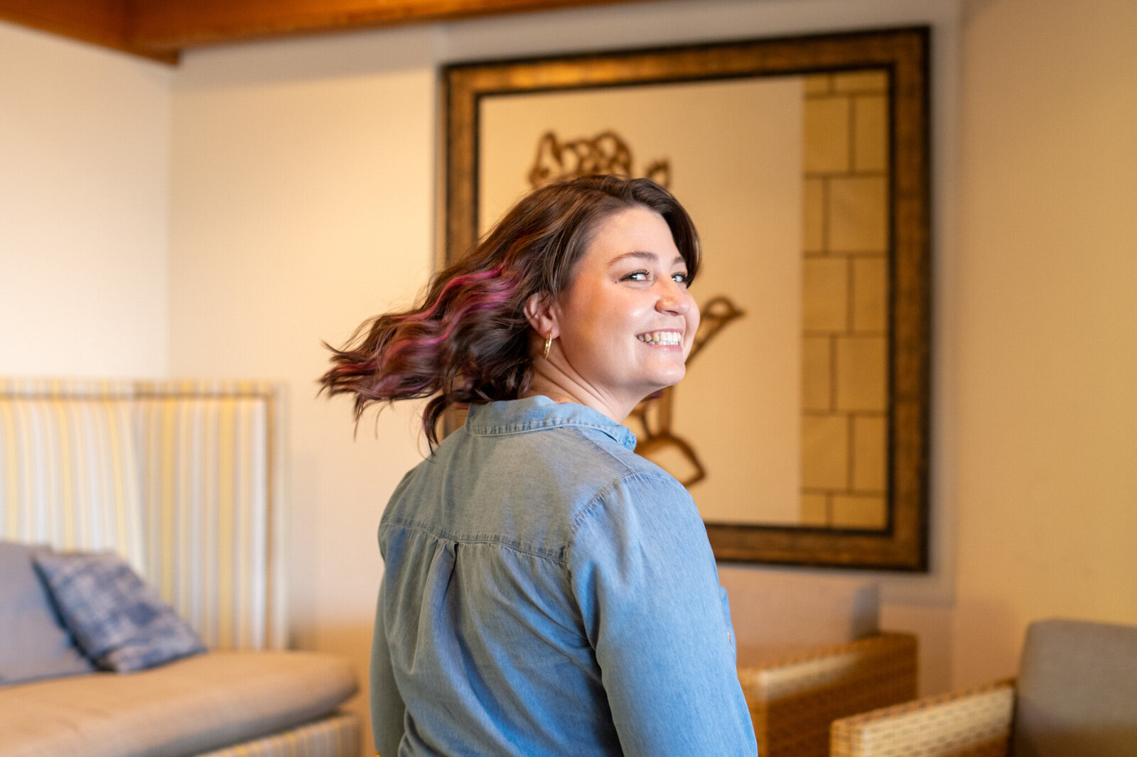 Smiling woman with curled hair wearing a denim top and yellow pants in a warm indoor setting, photographed by Vyrl Photo for Tucson brand photography.
