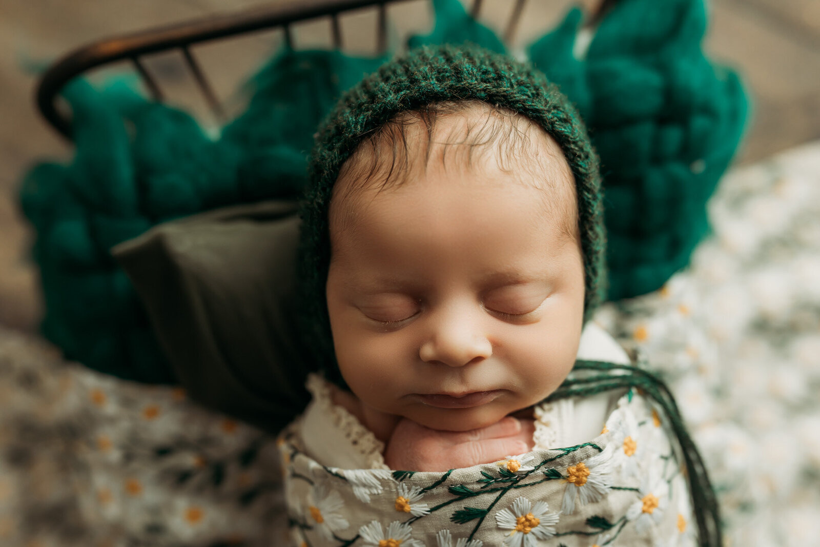 Baby girl in a green knit bonnet wrapped in a daisy blanket on a tiny bed in Harrisburg, PA