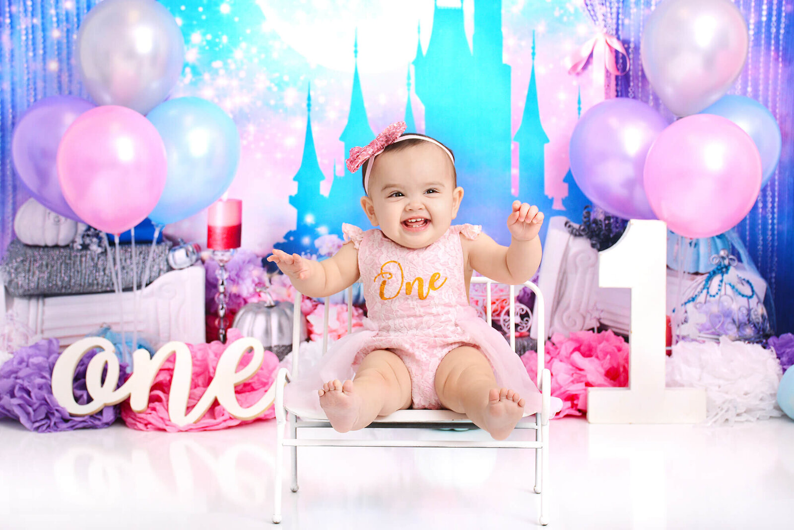 girl wearing a pink ONE romper smiles at her first birthday session