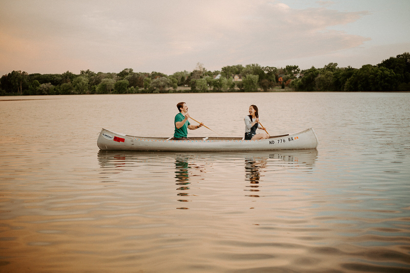 Couple canoeing in a minnesota lake at sunset during their engagement session