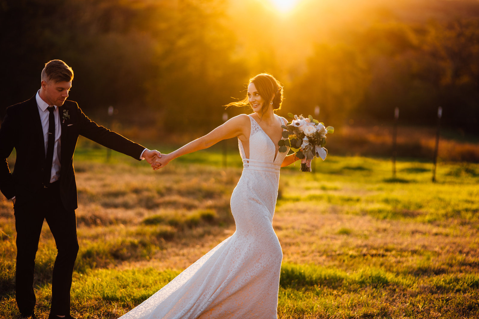 Bride leading groom through field during golden hour