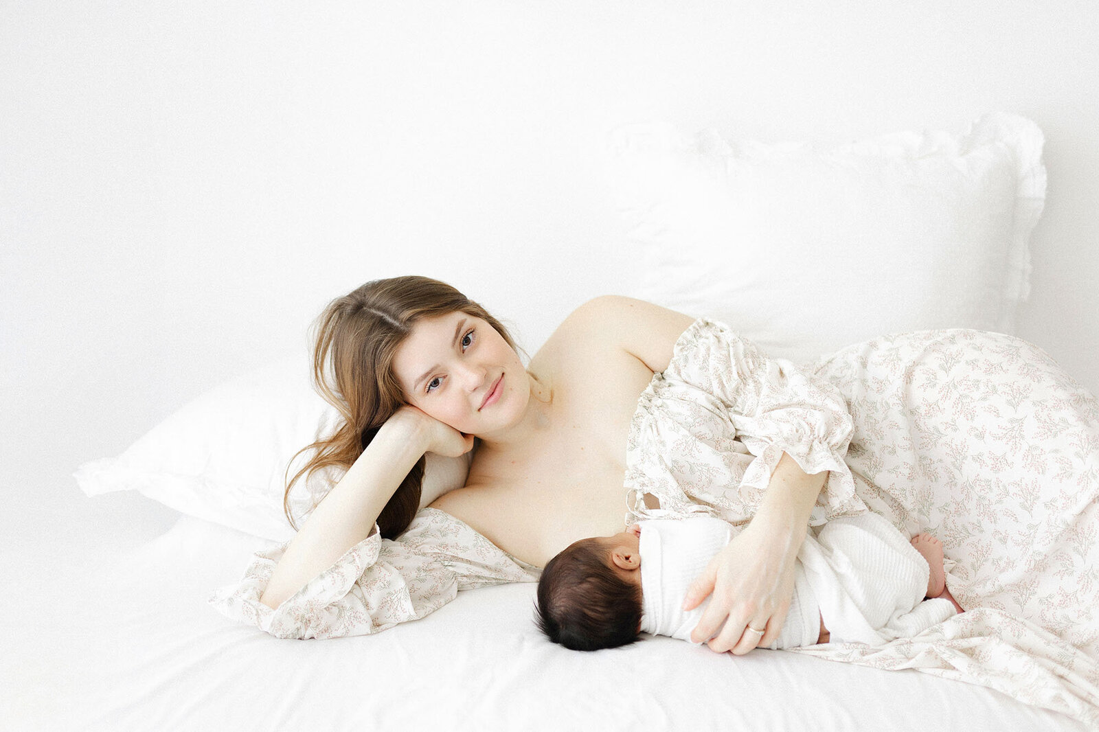 Mom laying on bed with newborn baby boy during professional portrait session