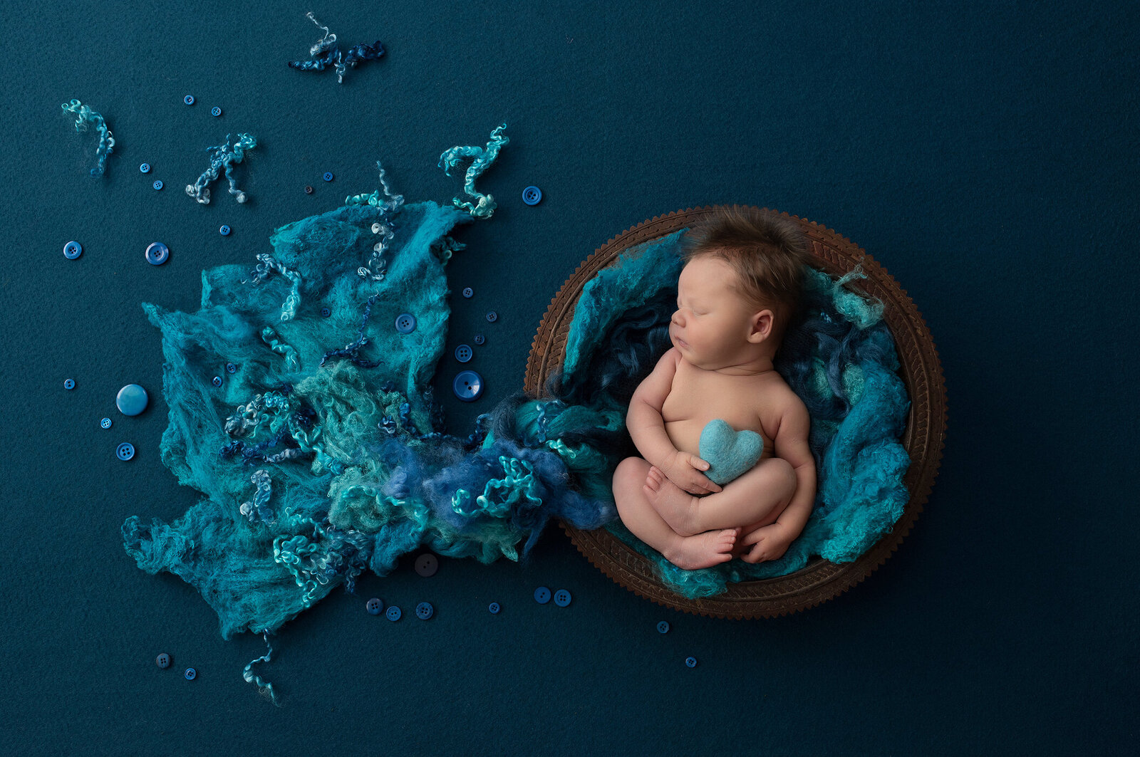 Newborn boy poses in basket wiht blue felt
