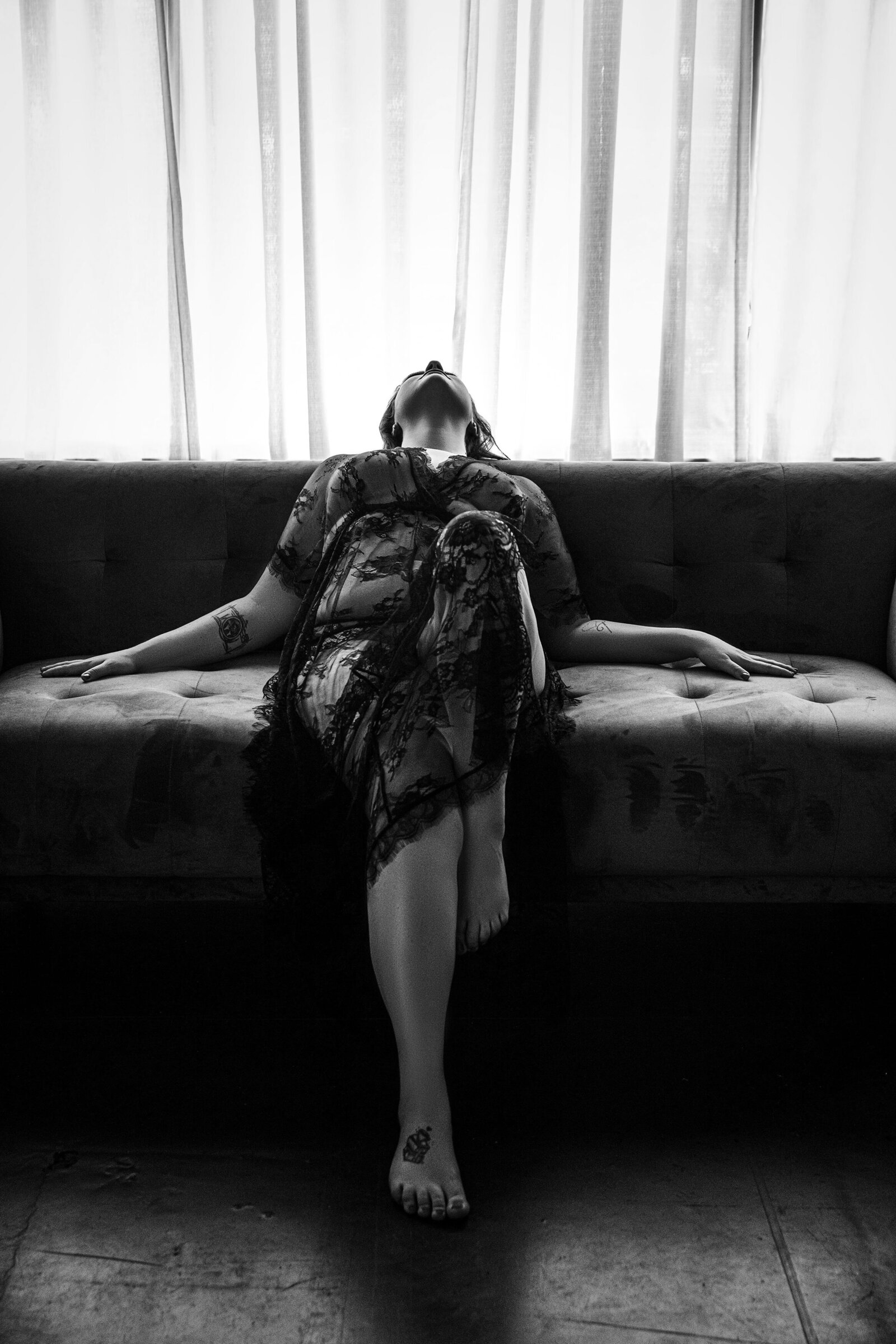 Silhouette of woman in black lace robe leaning back on sofa with hands to each side in Baton Rouge boudoir studio.