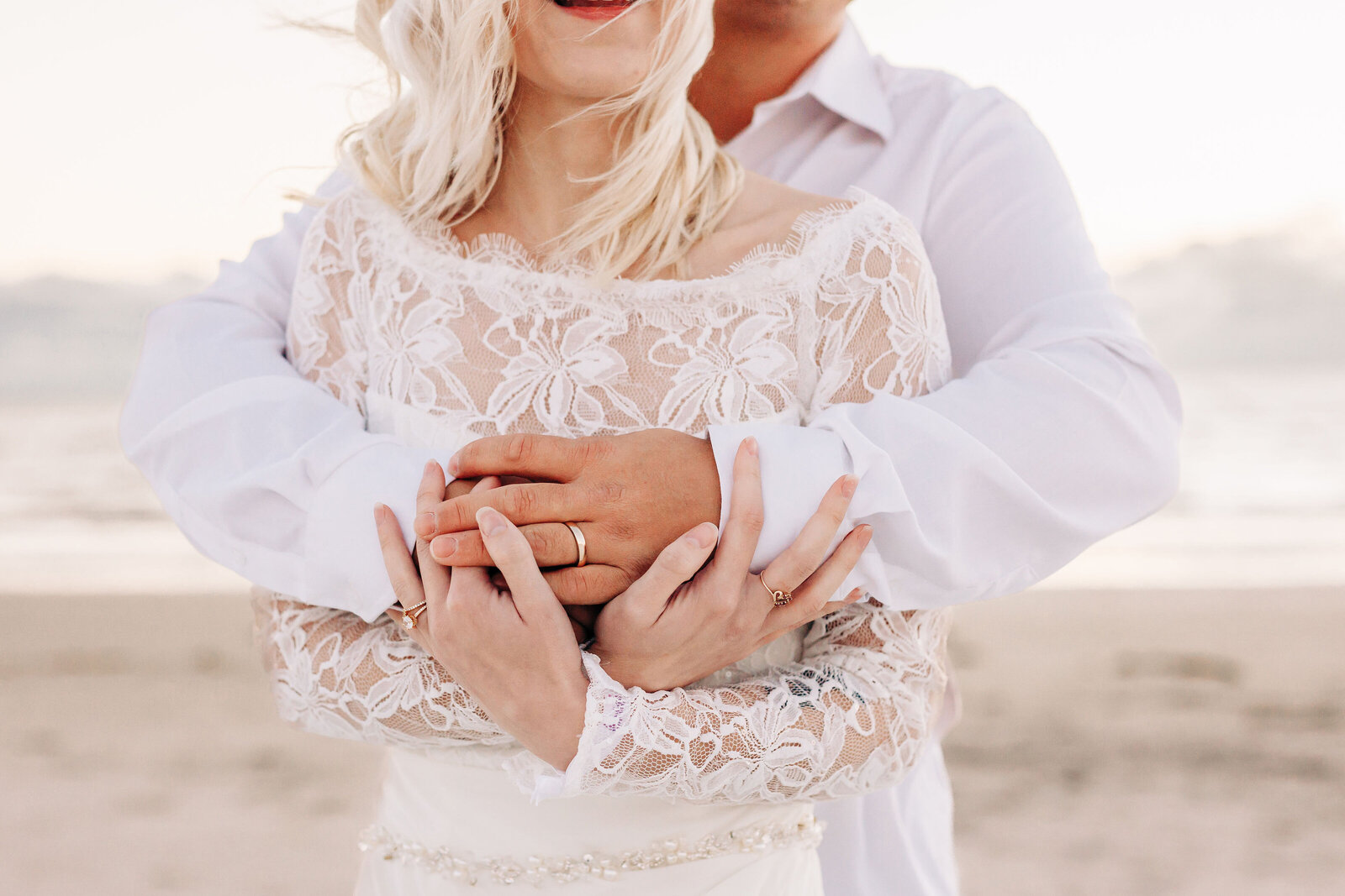 couple with hands wrapped around one another on the beach after their wedding