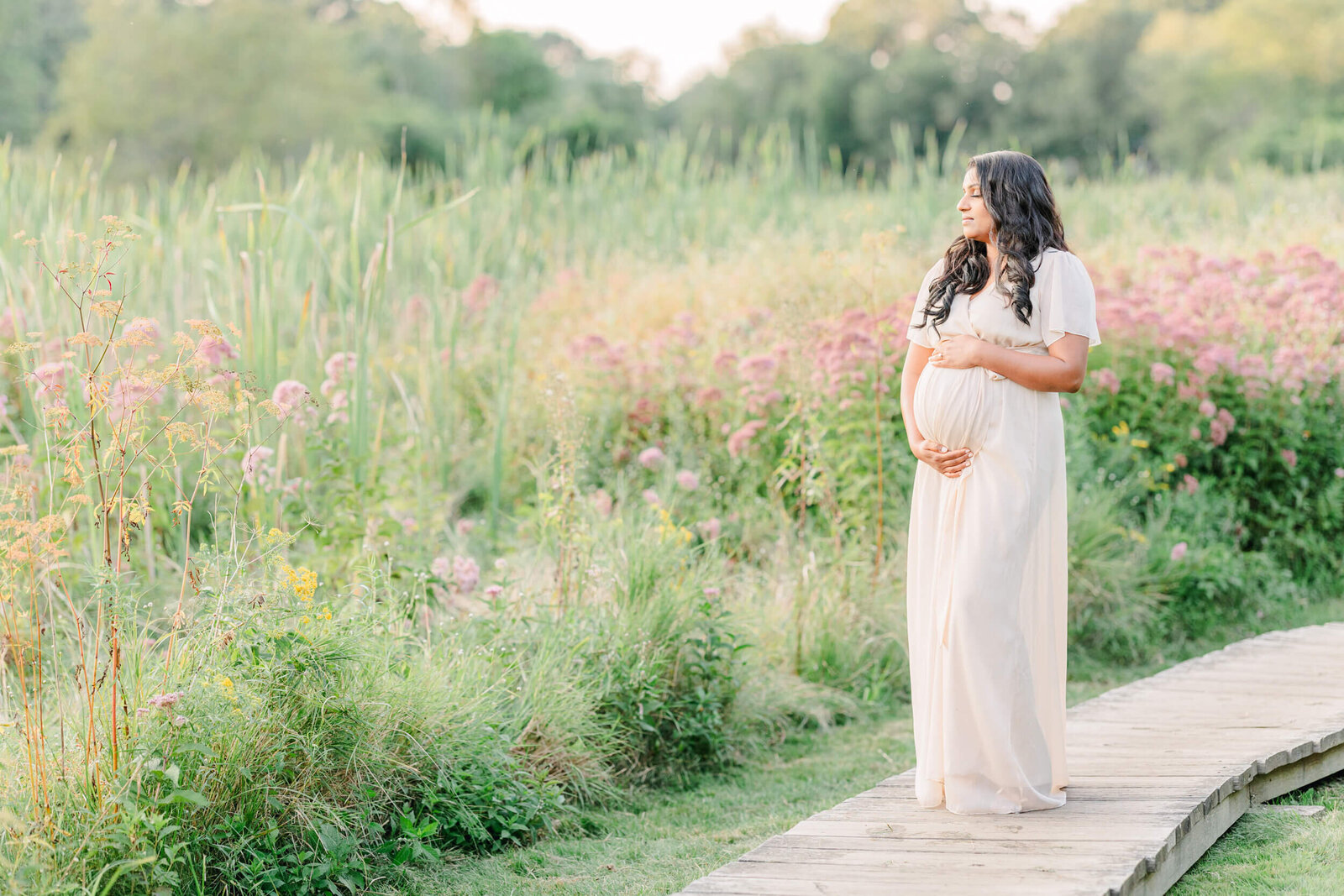 Pregnant woman cradles her baby bump in a field of wild flowers with her eyes closed