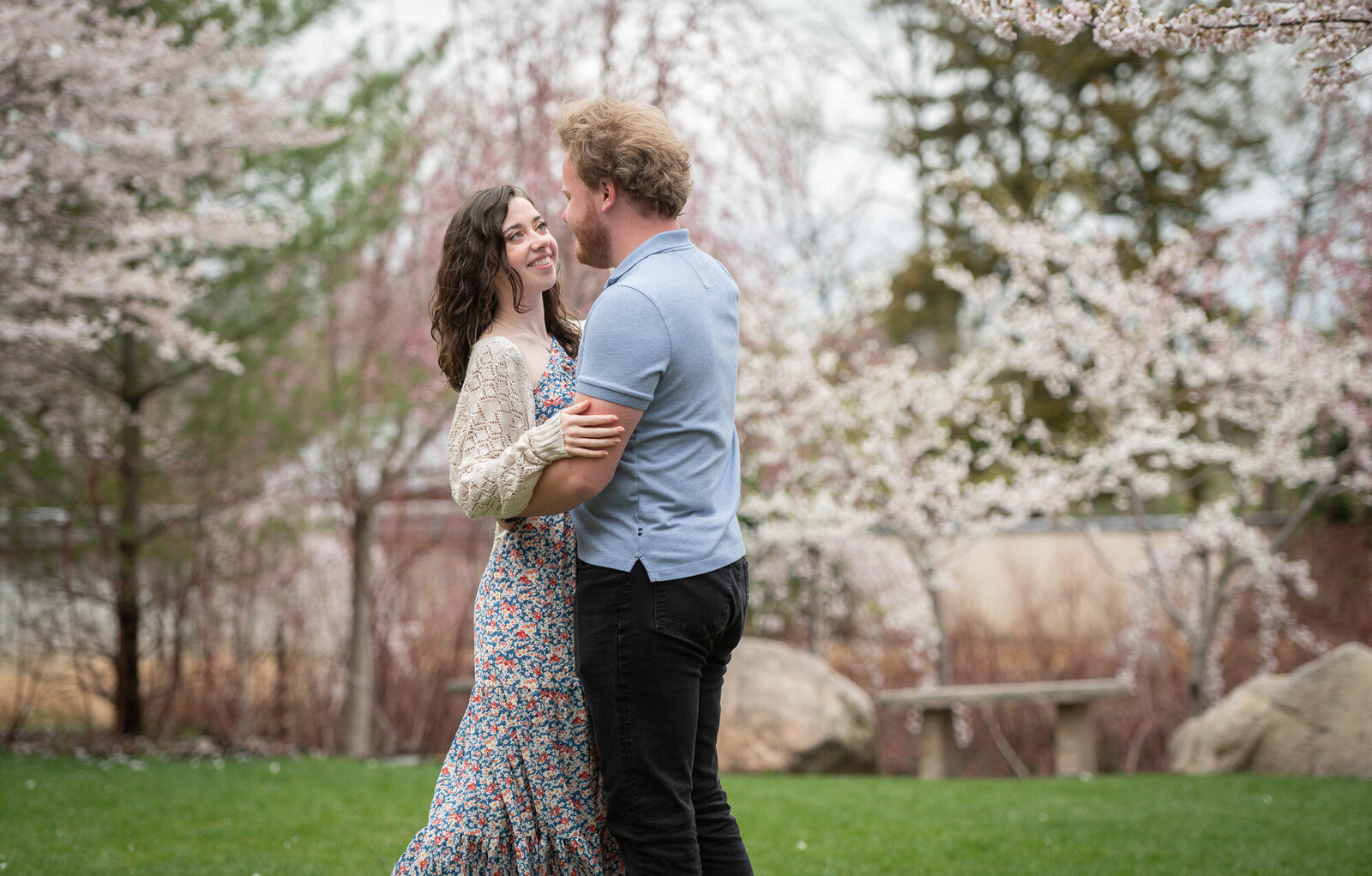 couple hug in front of cherry blossoms while she looks at him