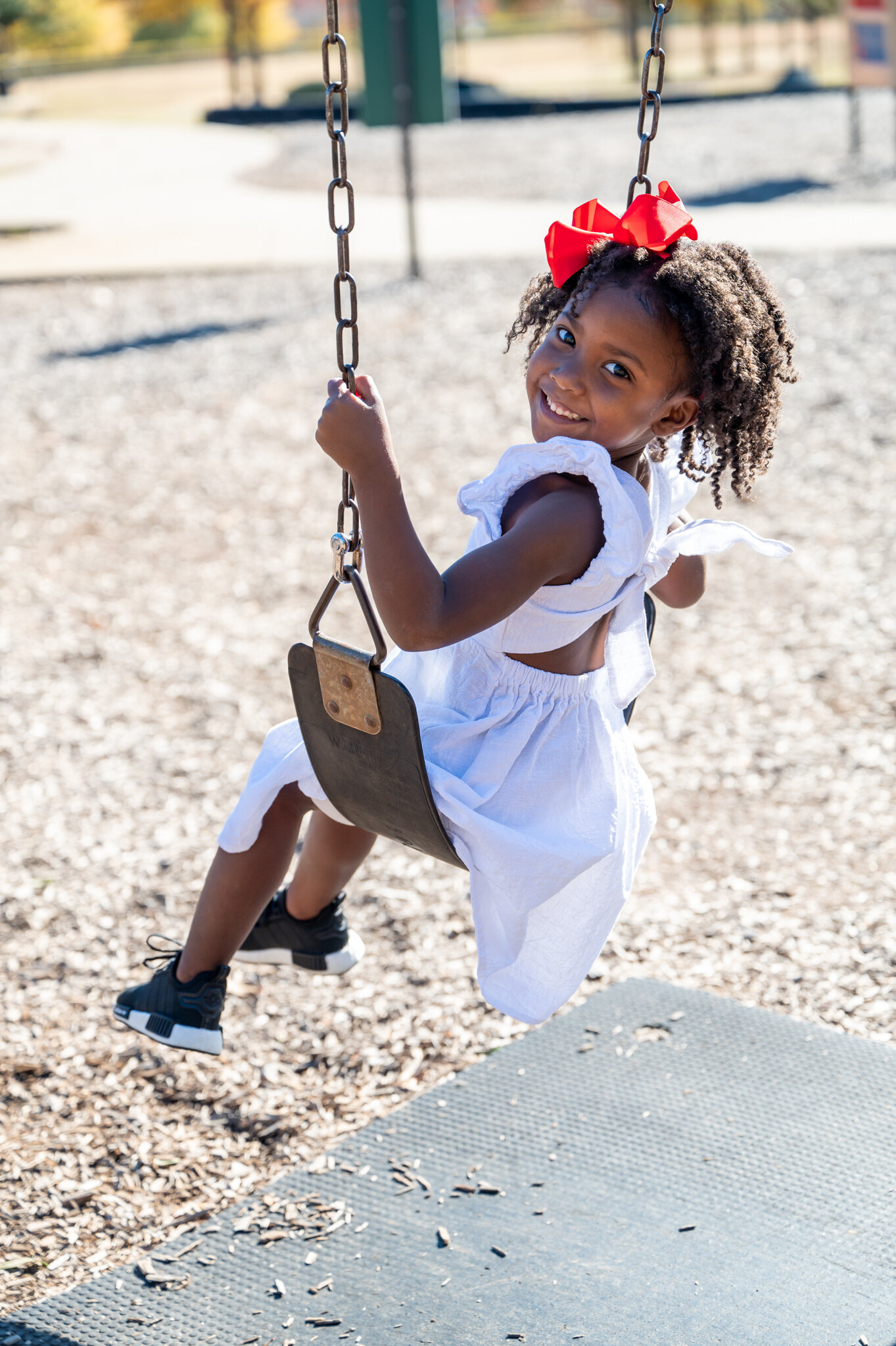 young girl on a swing at the playground smiling for the camera photographed by Millz Photography in Greenville, SC