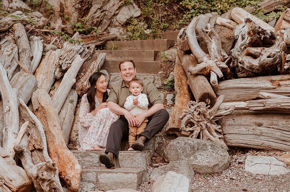 Family of three snuggling on wooden stairs on the beach with Vancouver Family Photographer