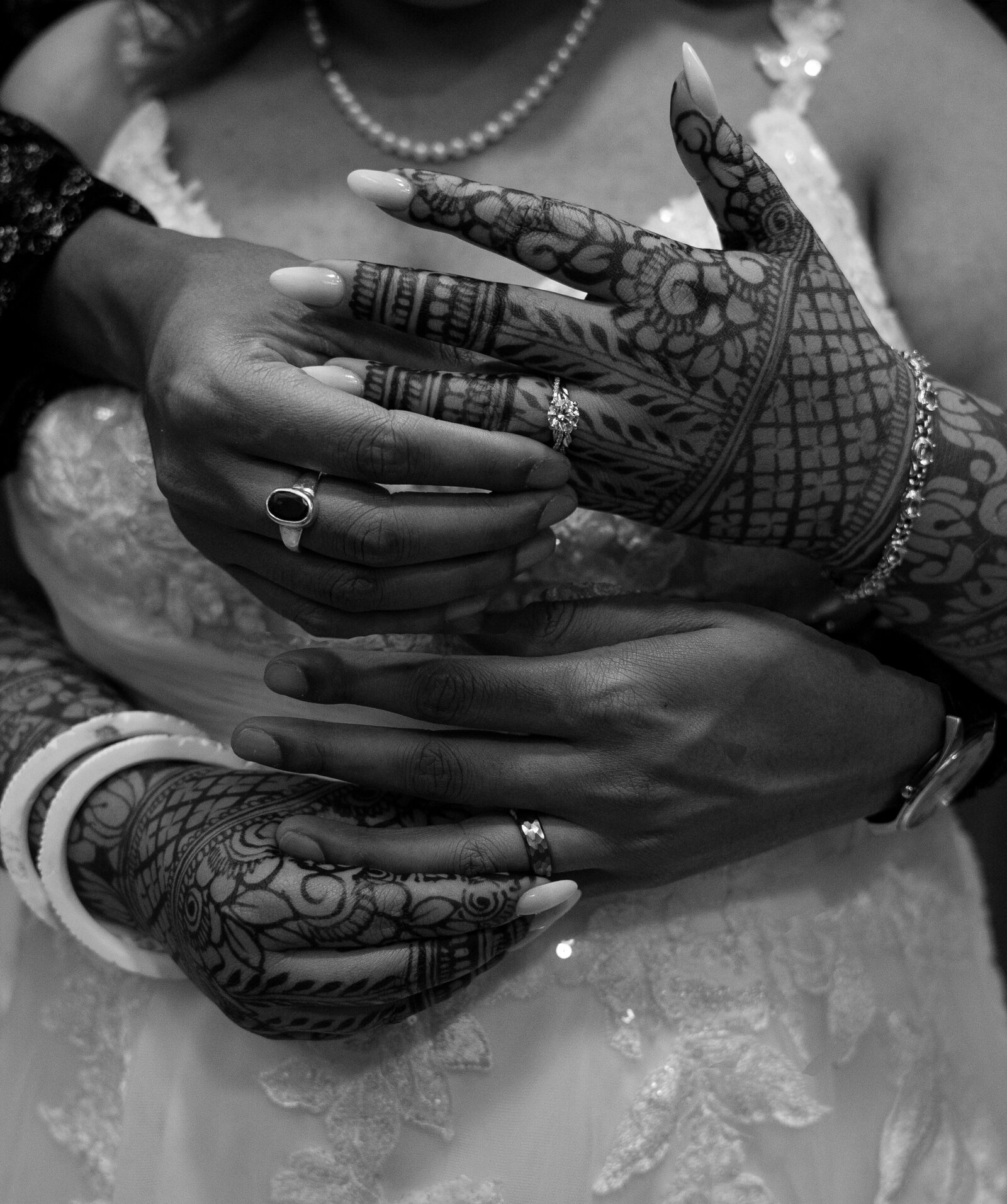 A couple on their wedding day putting their wedding bands on for a detail shot that shows off their rings and the henna art on her hands. 