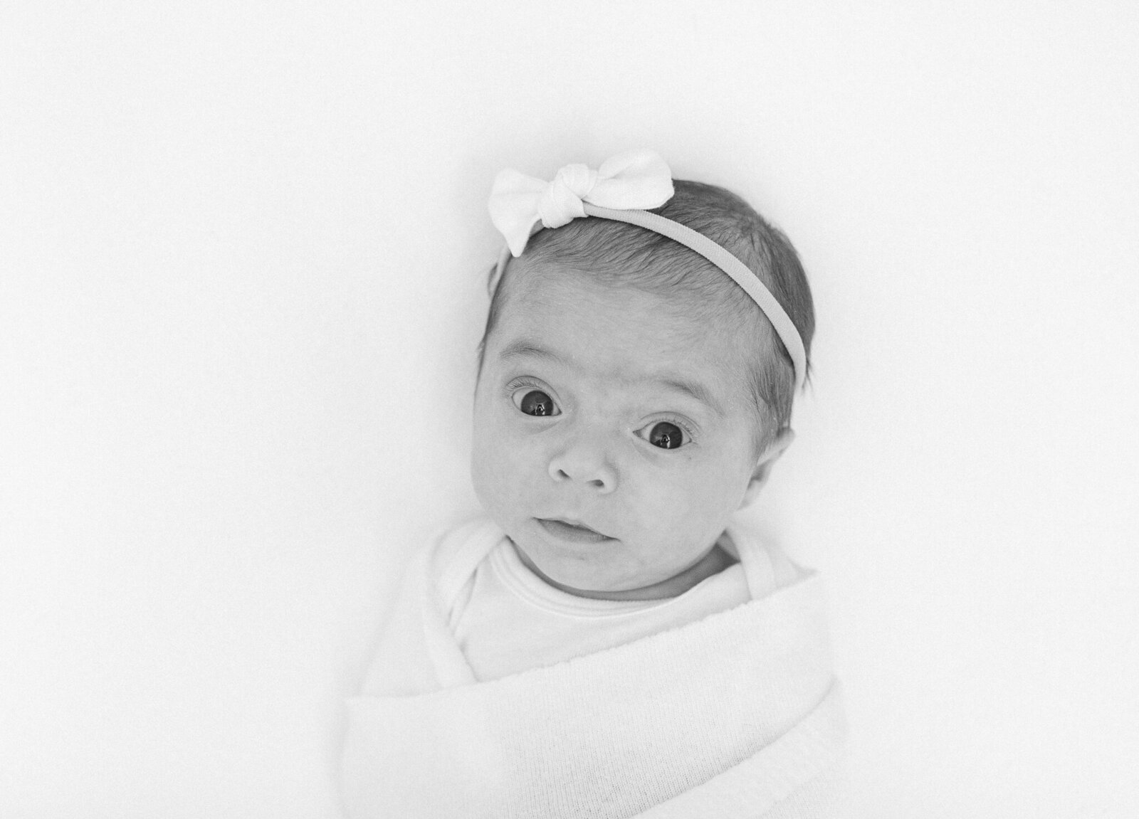 newborn baby girl wearing simple bow looks up at camera