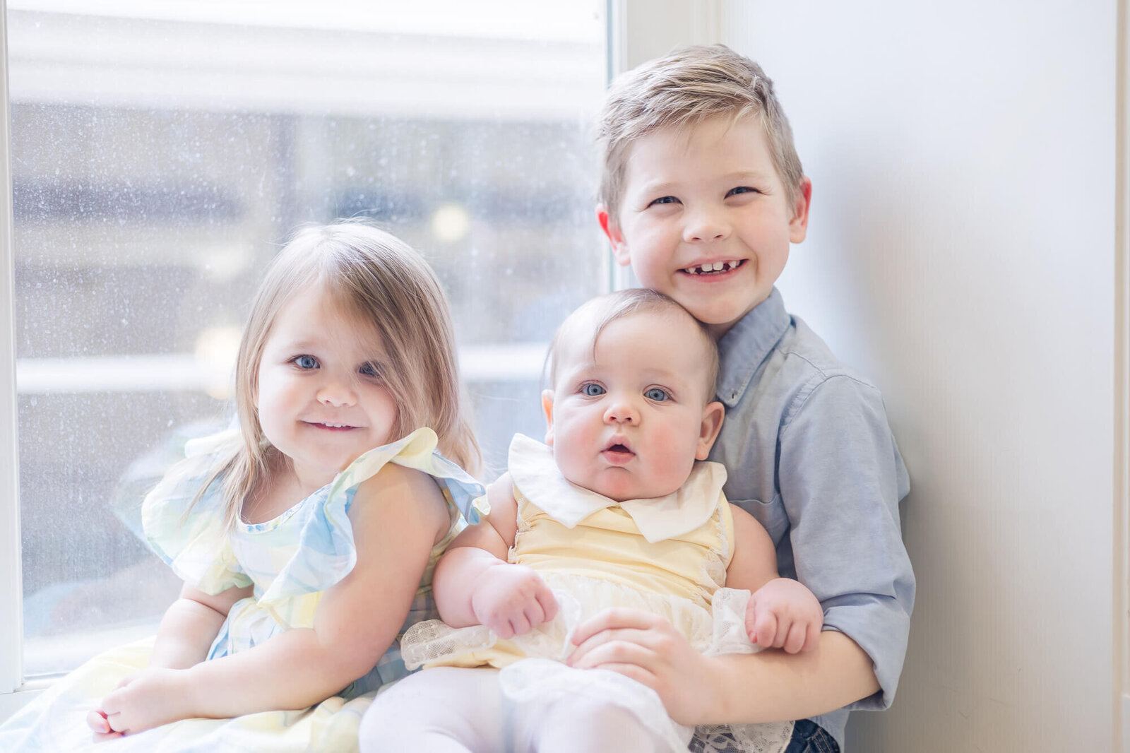 happy siblings sitting in a bright window