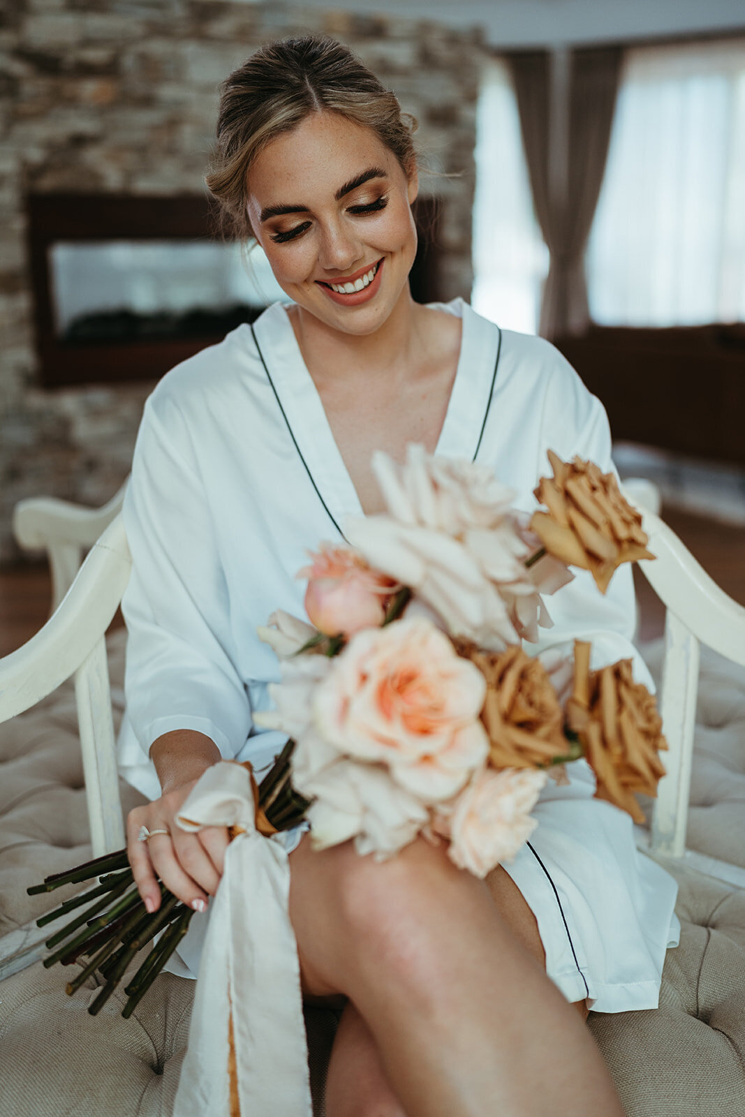 Gorgeous Bella Rae Bride Kristen gazing down at her flowers with a beautiful bronzed eye with peachy lips and low textured bun at Austinvilla Estate captured by  Daniel Chafer Photography
