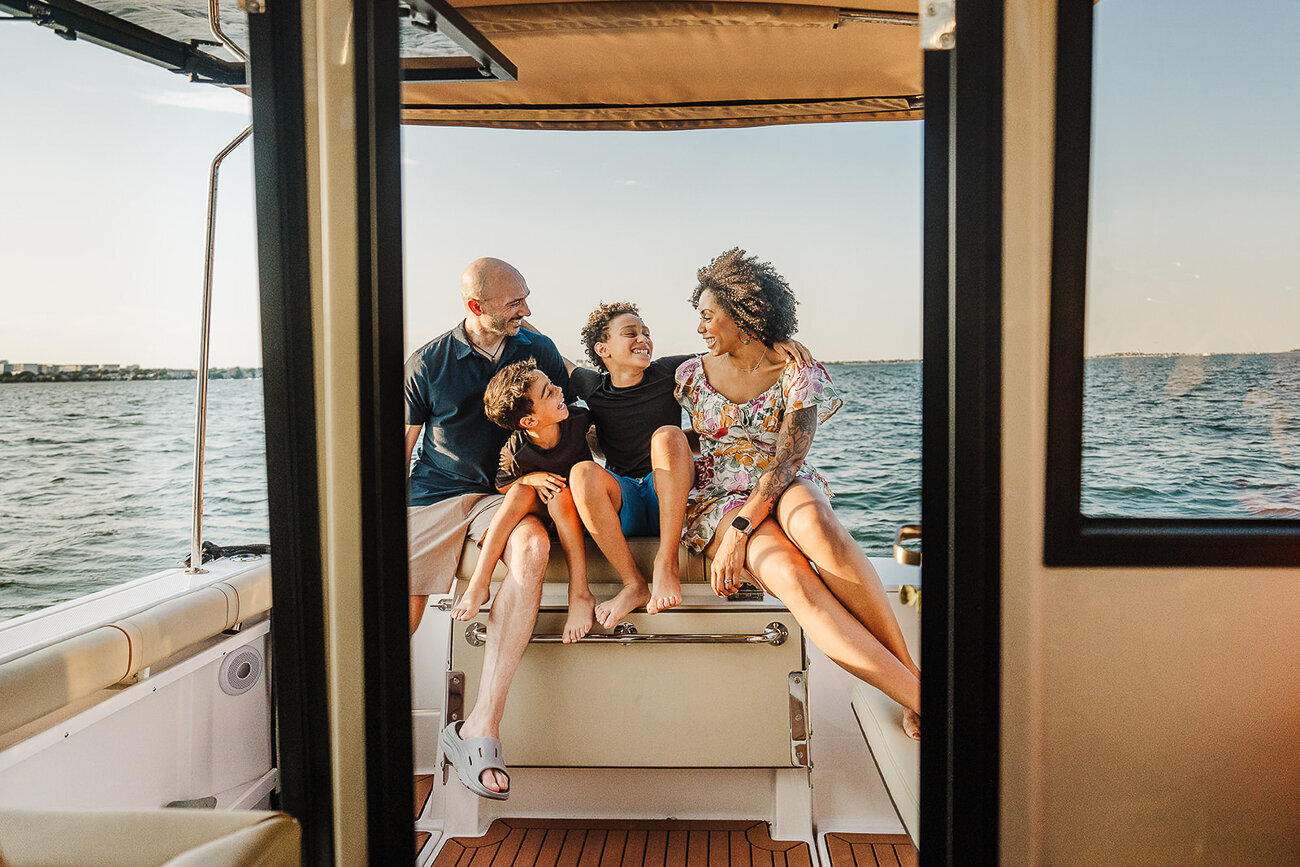 family of four sits at the back of a boat for sailing family photo session in boston harbor