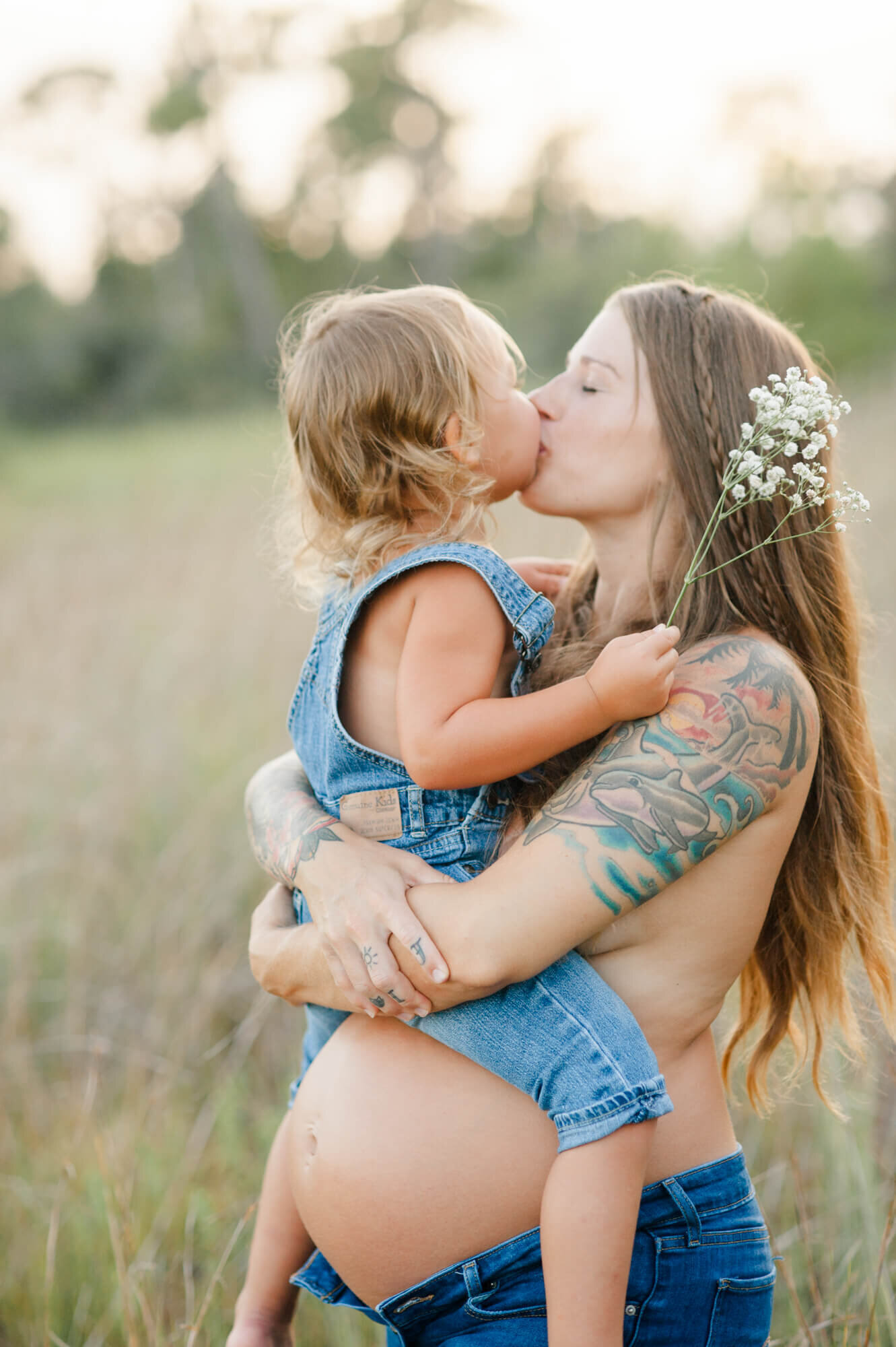 Expectant mother holds her oldest daughter on her belly and kisses her at sunset
