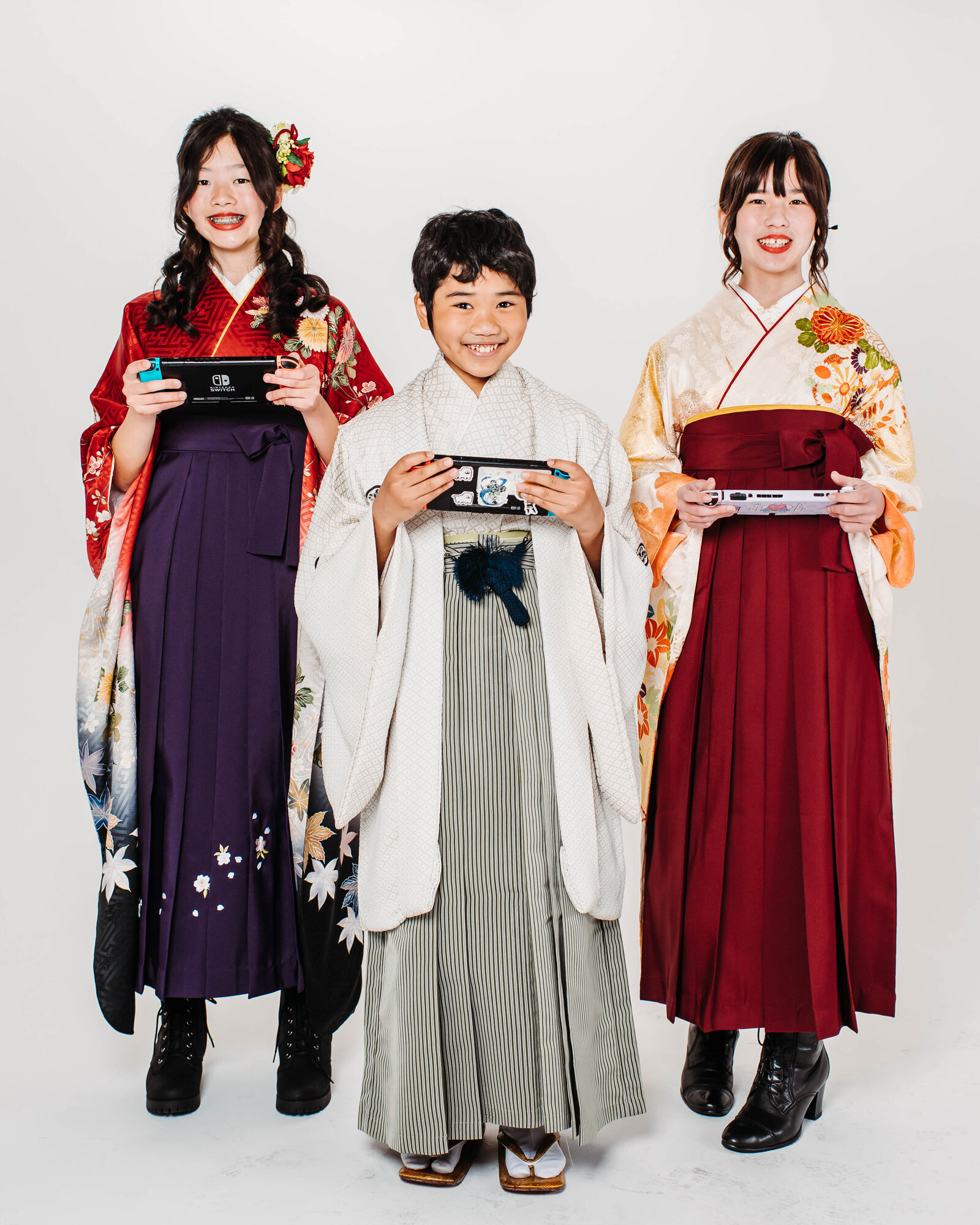 Three students in hakama and kimono holding Nintendo Switch consoles during graduation photo | 卒業式 袴と着物 姿 任天堂スイッチを持つ 生徒たち