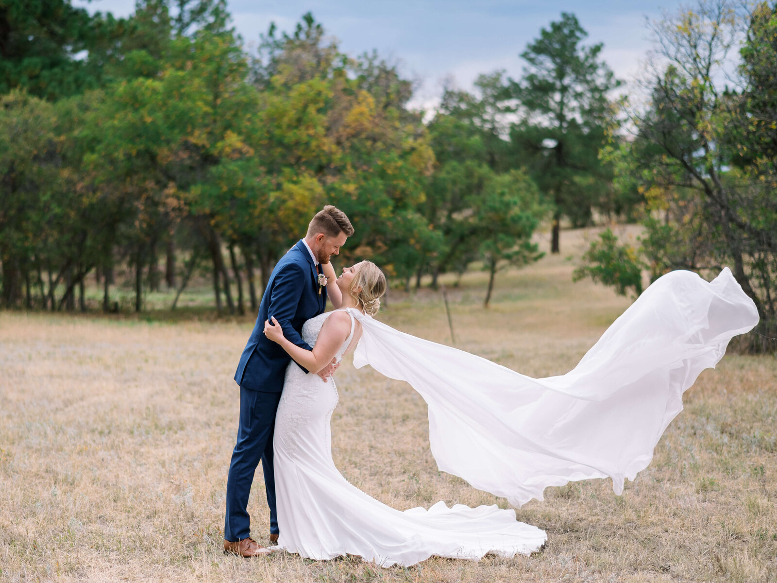 Blonde bride's wedding cape flies in the wind behind her while her new husband dips her before a kiss
