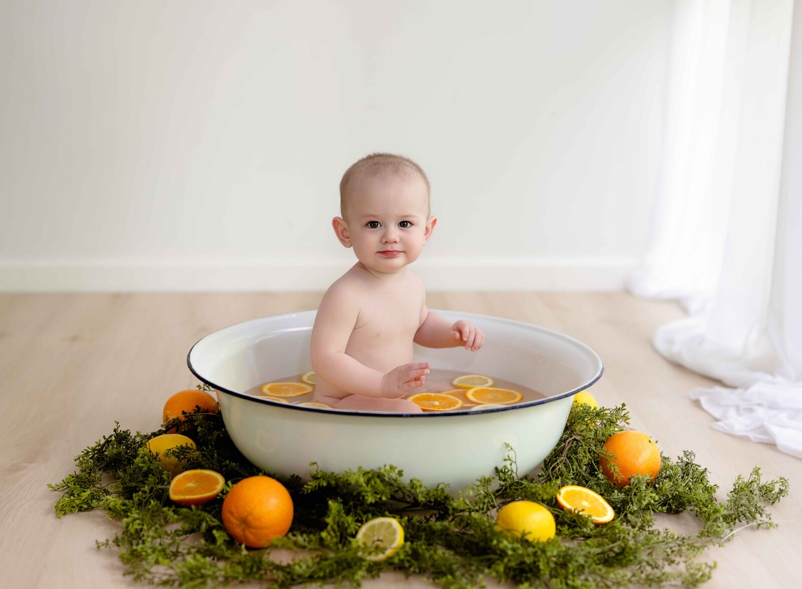 Baby sitting in basin tub with oranges and lemon slices in water and greenery on outside of basin. Baby Photo taken by Jenni Nikki Photography at Atlanta Photo studio.