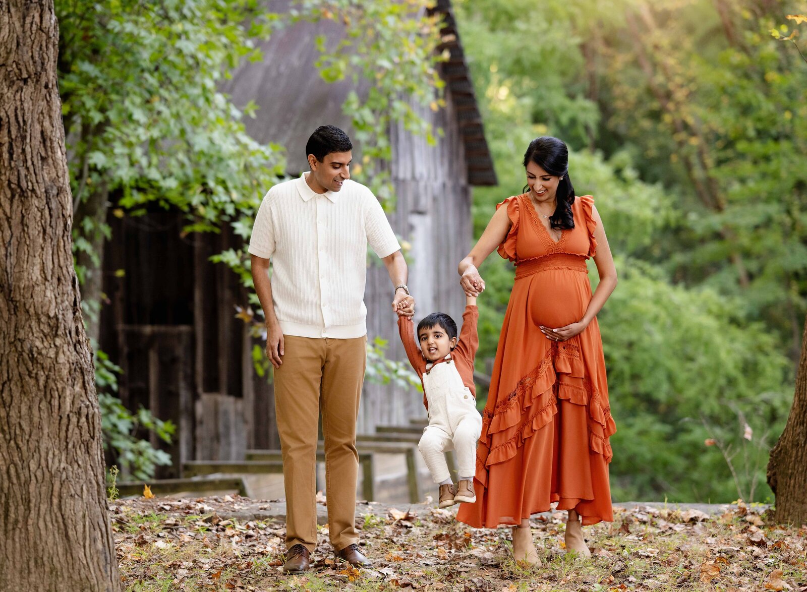 Parents swinging toddler child as they are walking in the woods and smiling at him. 