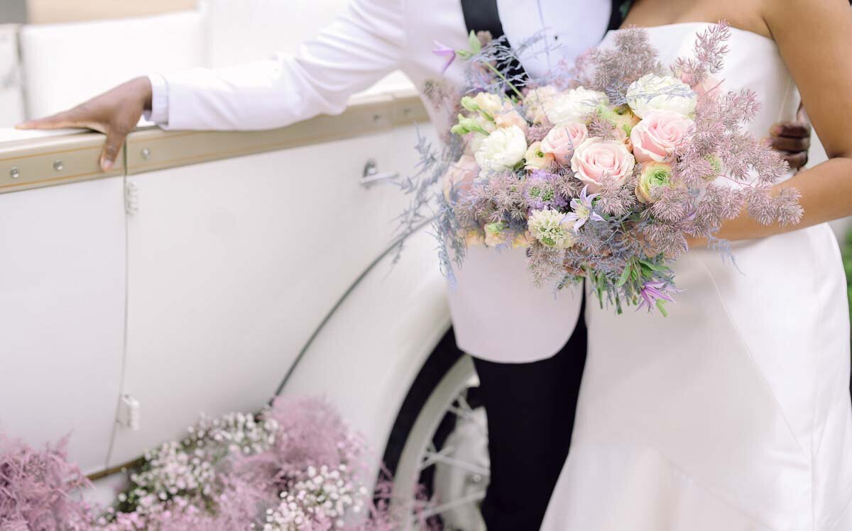 wedding photo of bride and groom leaning against sports car showing brides bouquet