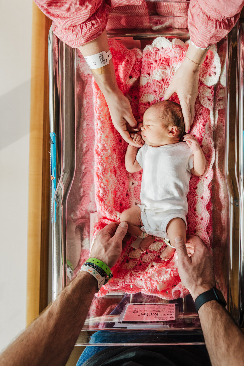 parents lean over hospital bassinet and touch new baby