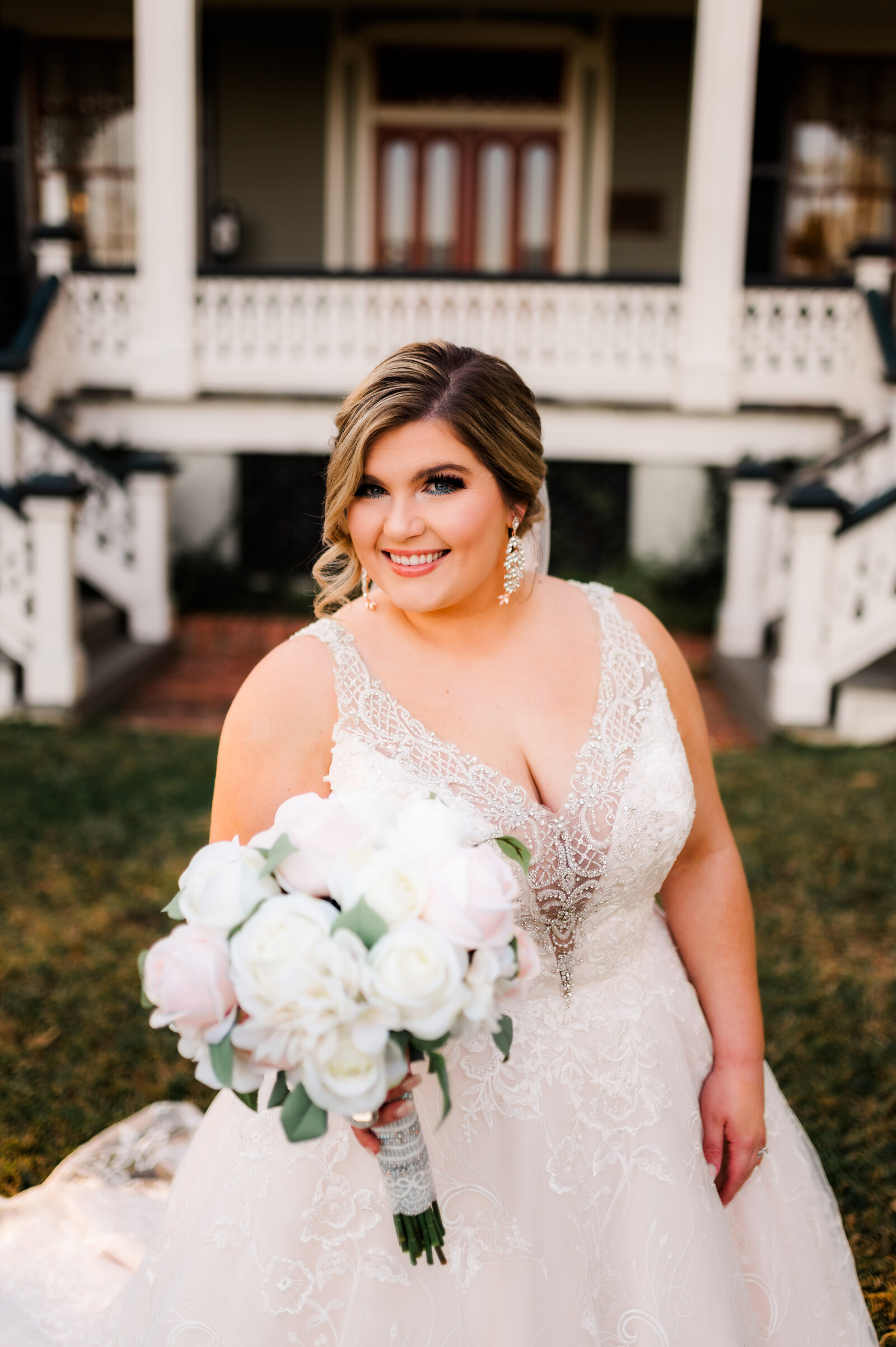 little rock ar wedding photos of bride outside on a lawn holding her white florals wearing her lace dress and smiling up at the camera