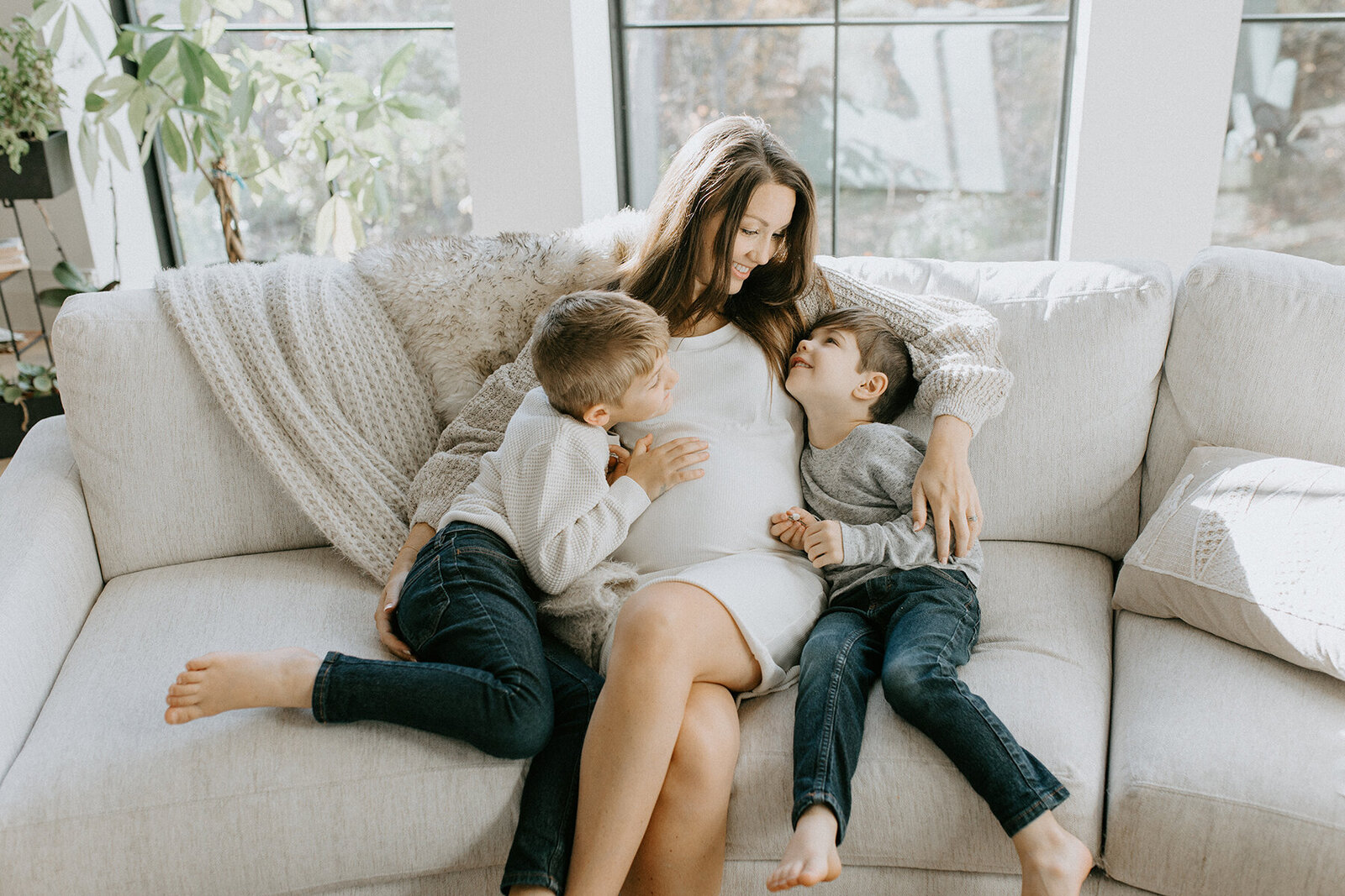 A Lafayette, Indiana indoor maternity photo session. A pregnant mom sits on a couch with her two small boys. 