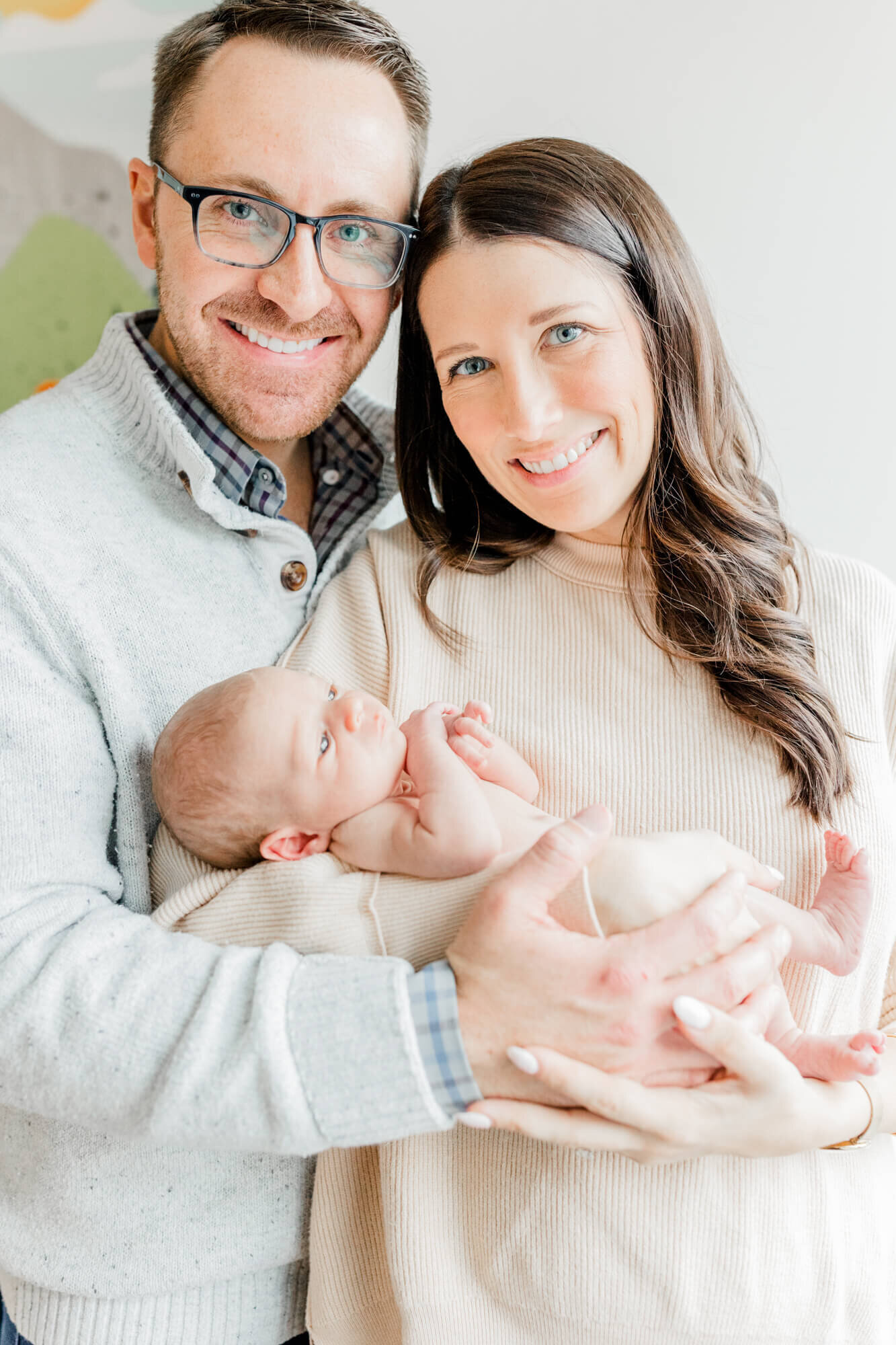 Portrait of a smiling mom, holding her newborn, and dad