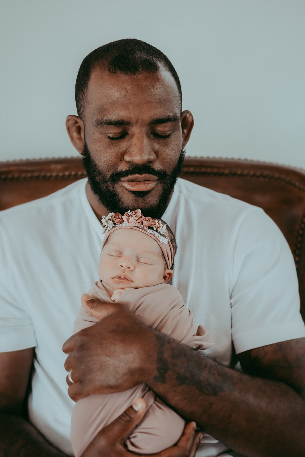 father holds swaddled newborn under chin facing camera