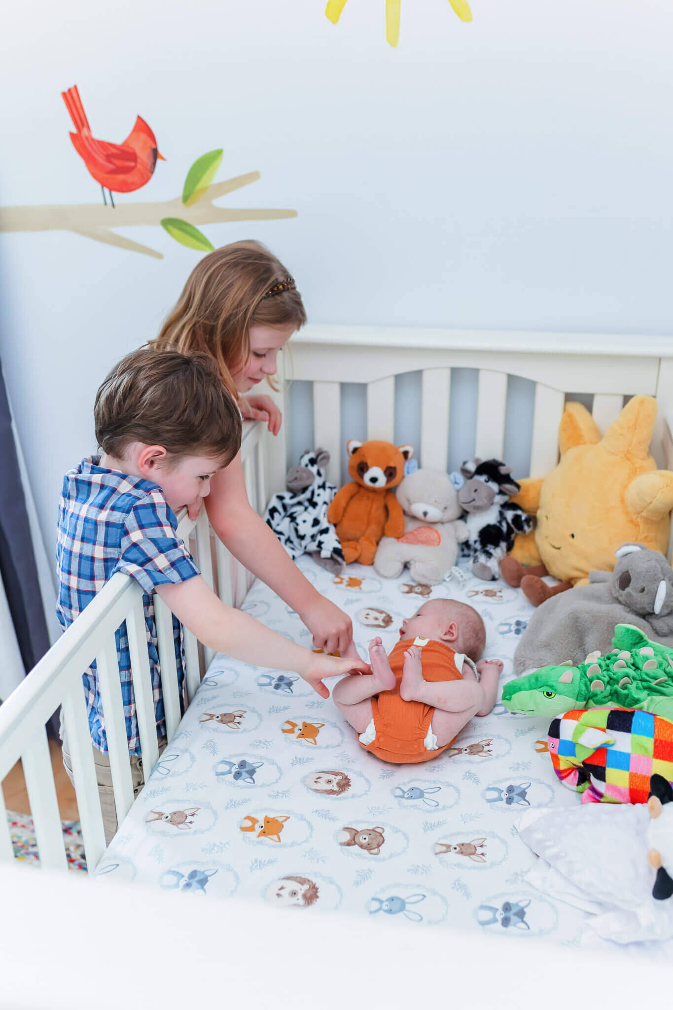 A big brother and sister looking over the side of the crib at their newborn brother.