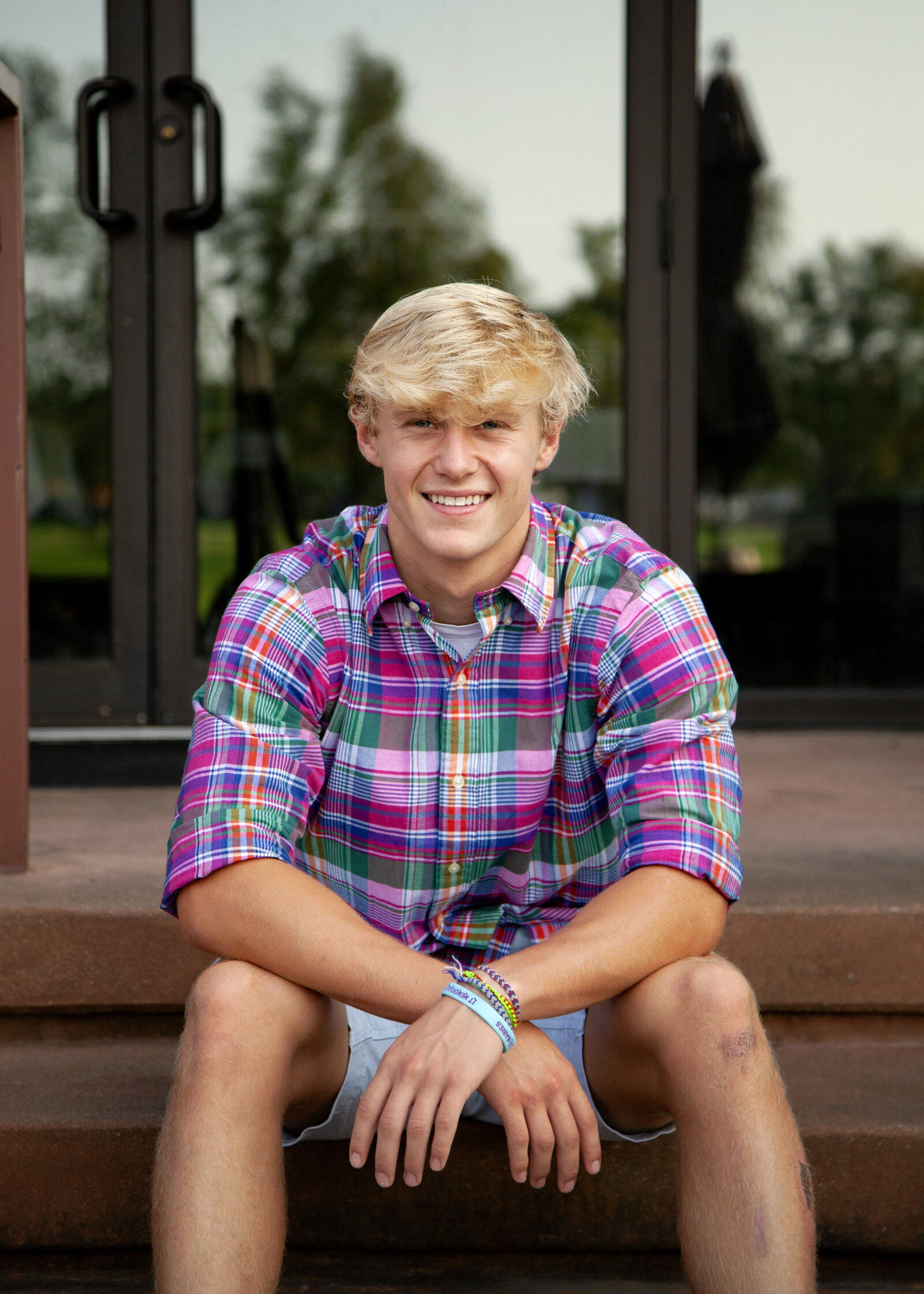Senior boy in pink shirt sitting on stairs.