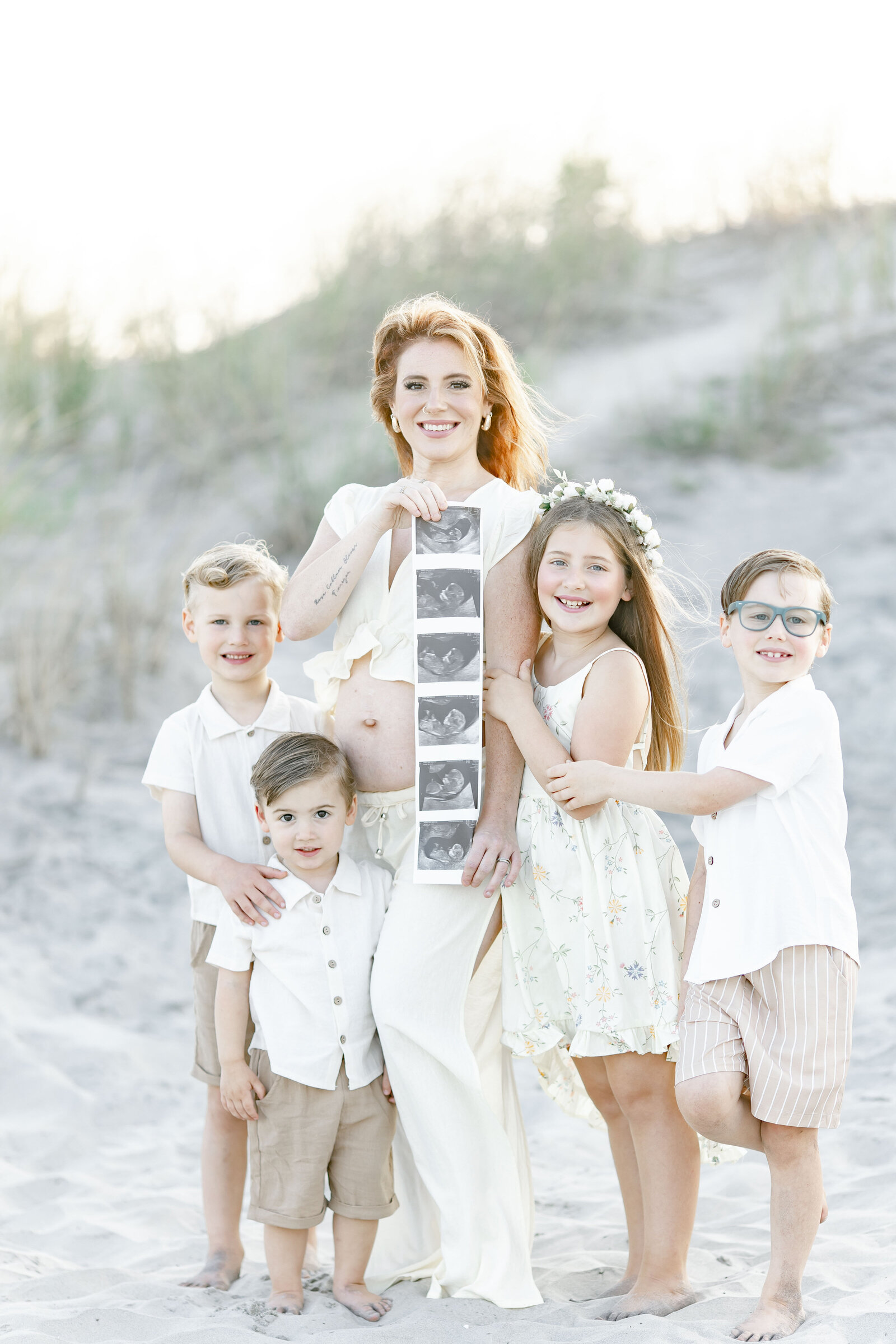 photo of mom holding an ultrasound surrounded by her four kids on the ocean city beach taken by photographer ally kimpton