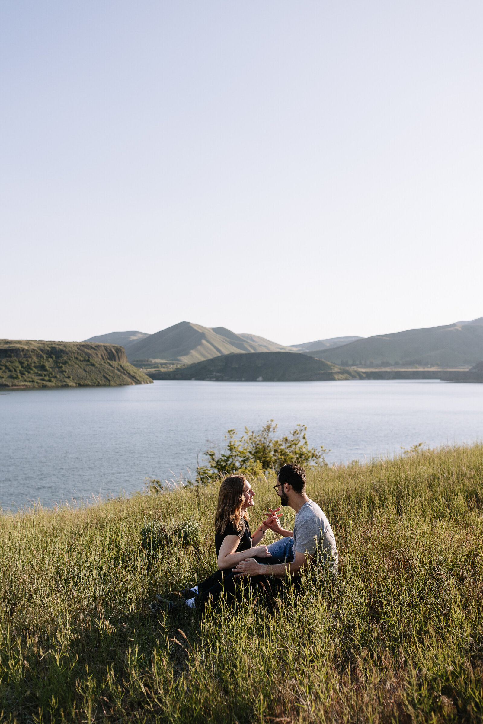Engaged couple laughing together in tall grass overlooking Lucky Peak Lake in Idaho