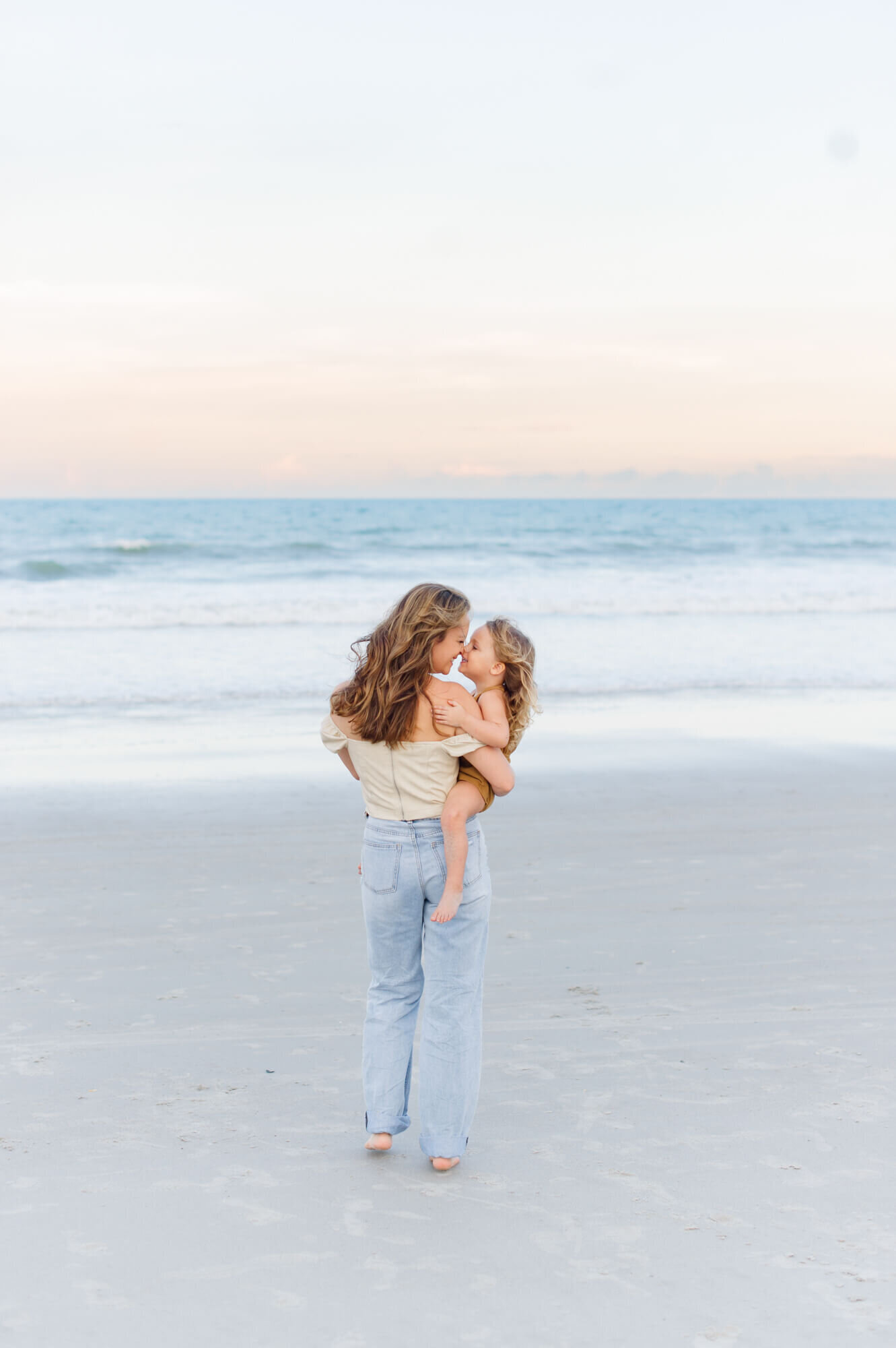 Mom and daughter standing with the beautiful waves in the background giving eskimo kisses on Melbourne Beach, Fl