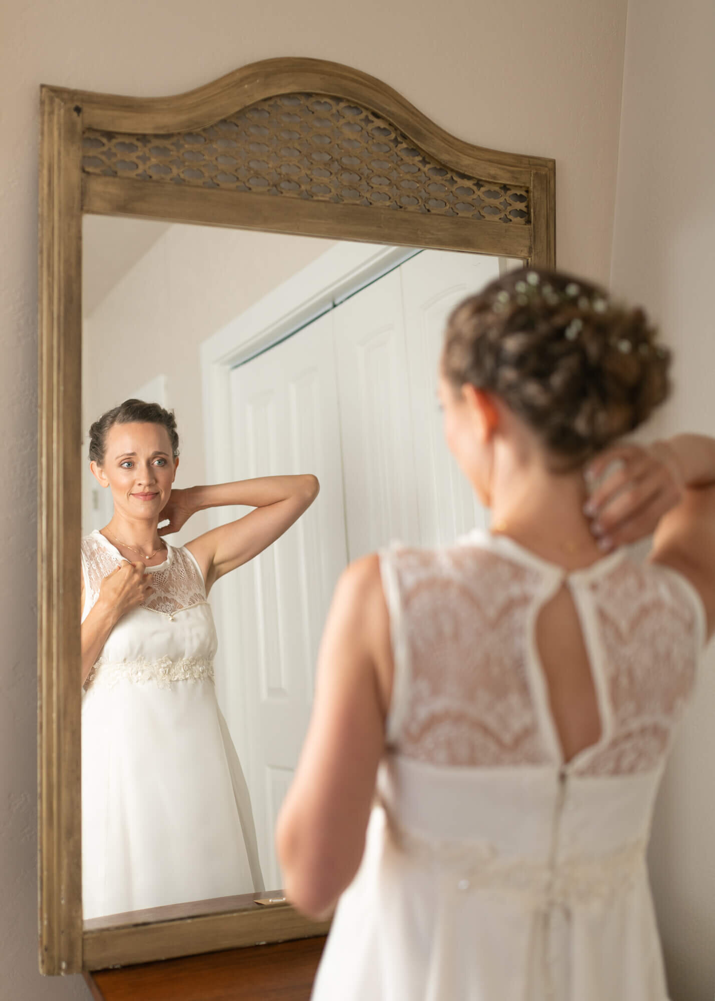 Bride looking in mirror adjusting her necklace