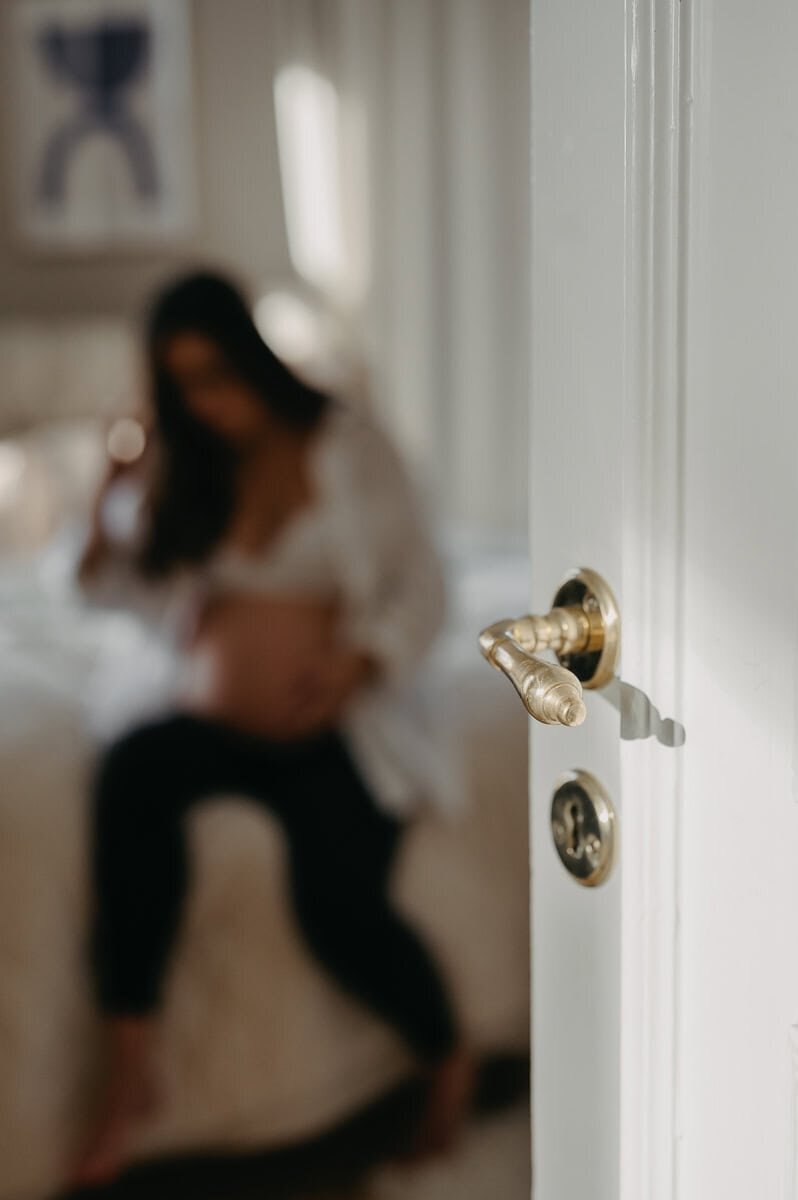 Blivande mamma sitter på sängen med en halvt öppen dörr i förgrunden.