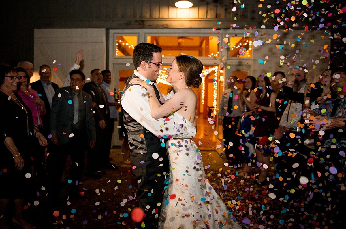 The bride and groom kiss as they exit their wedding venue amongst a celebration of confetti