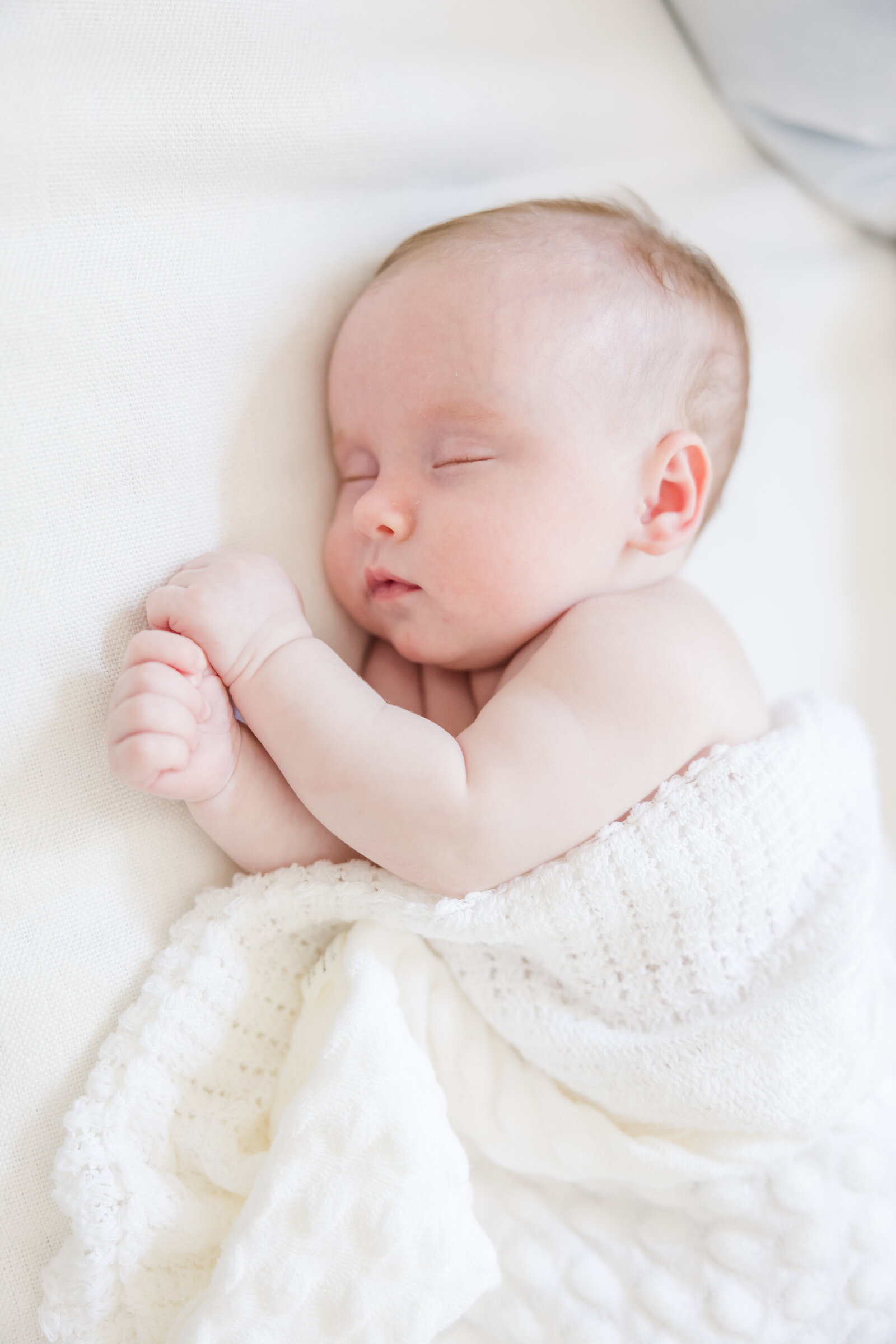 Newborn baby asleep covered by white blanket.