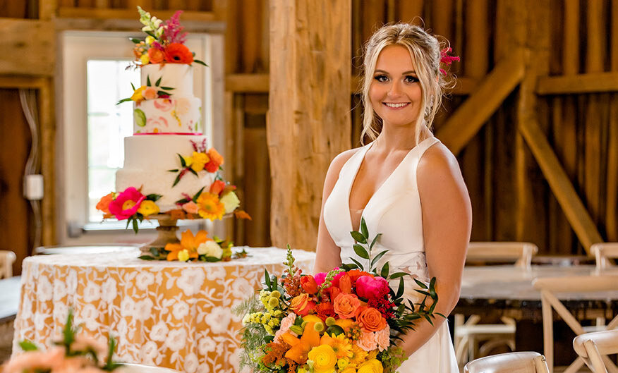 Bride holding a bouquet in front of a cake in a barn