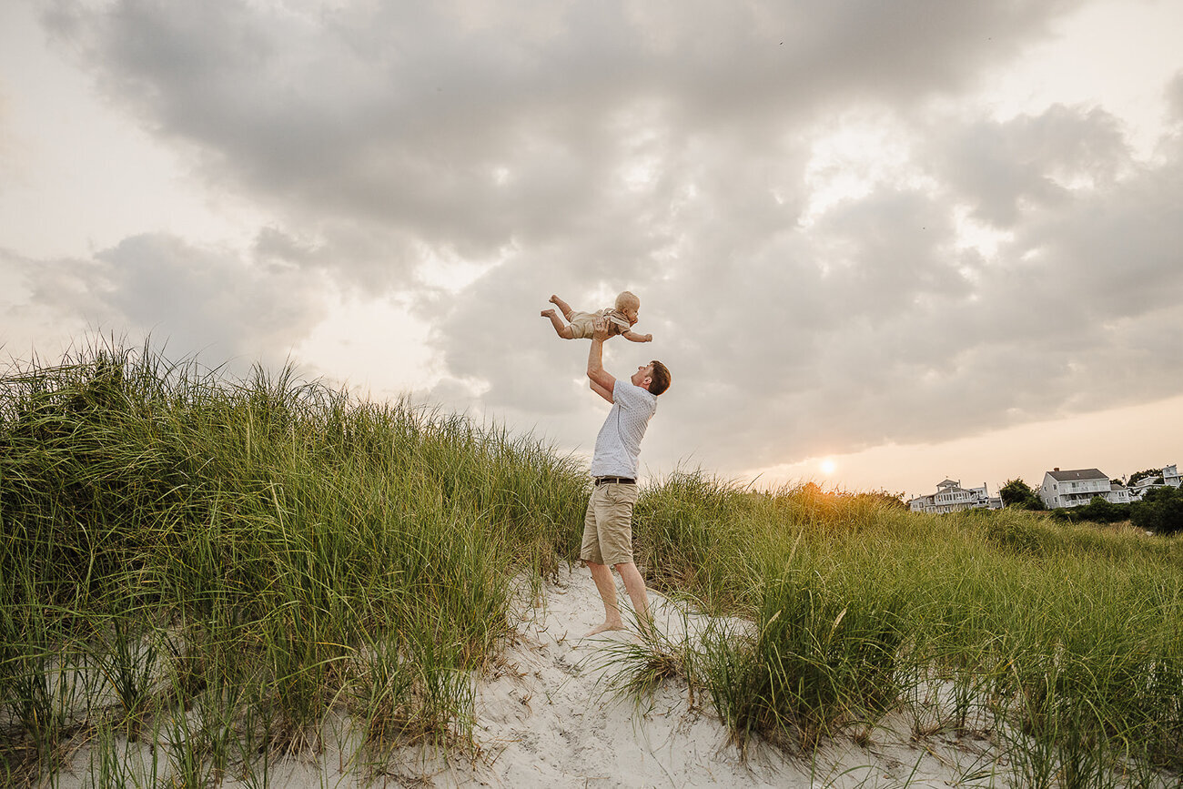 dad holds son to sky while standing in beach dunes