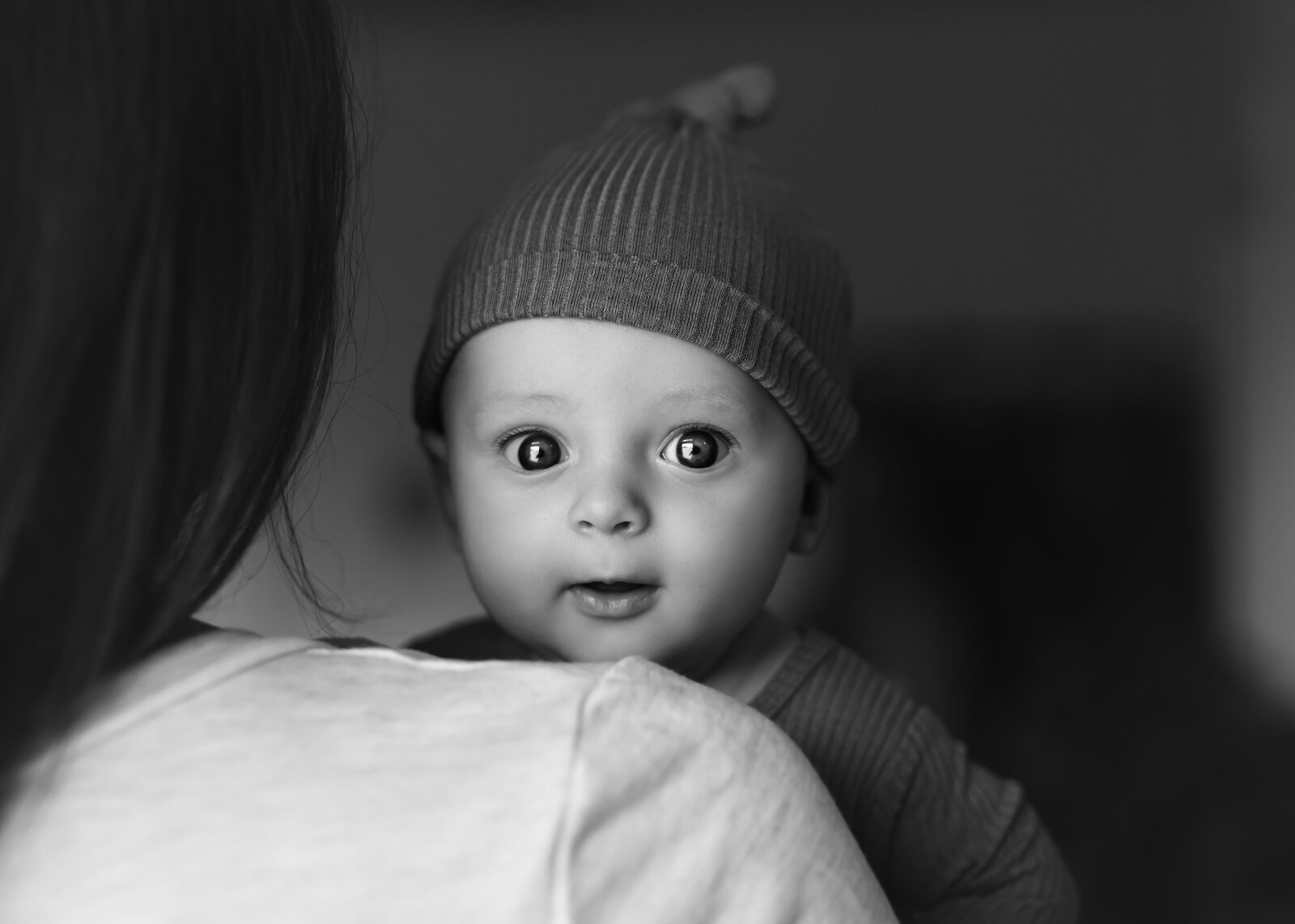 black and white of baby girl wide eyed looking over mom's shoulder