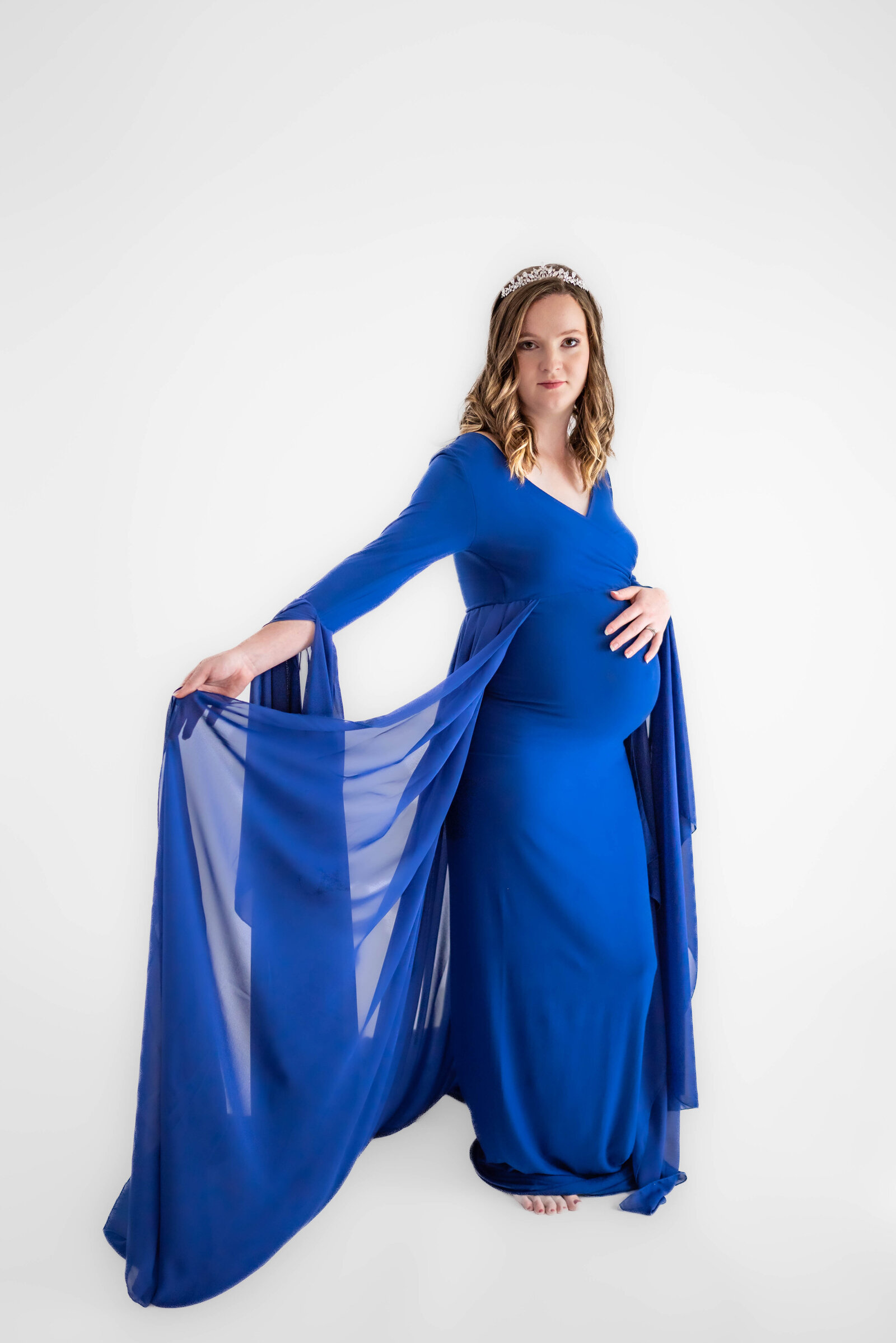A pregnant woman in a royal blue dress  holding her stomach and posing for her maternity photos in Huntsville Alabama