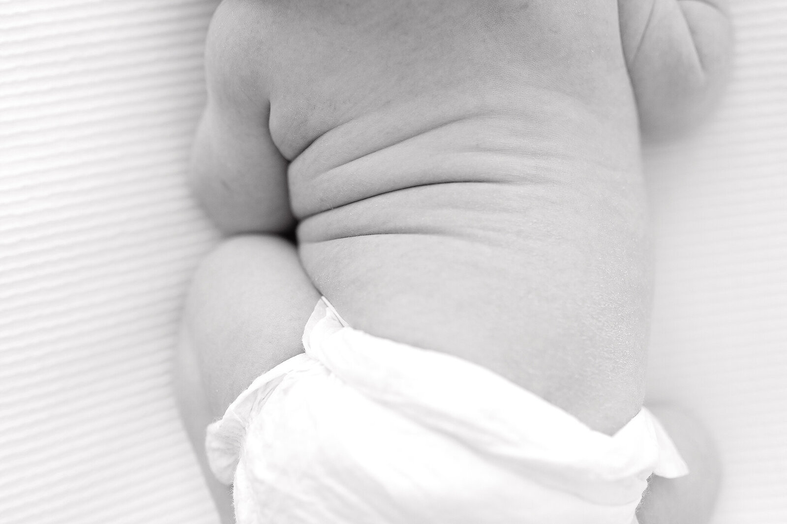 Black and white close up of newborn baby stomach rolls while curled up on a white blanket