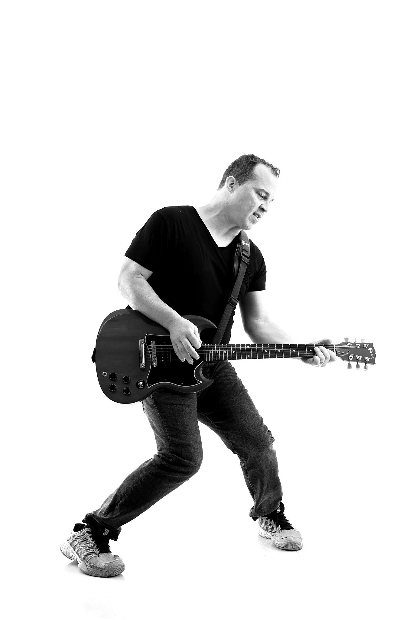 A man wearing a black t-shirt, jeans, and sneakers plays an electric guitar in a dynamic pose against a plain white background—perfect for any Jacksonville band photographer seeking striking music photography Jacksonville images.