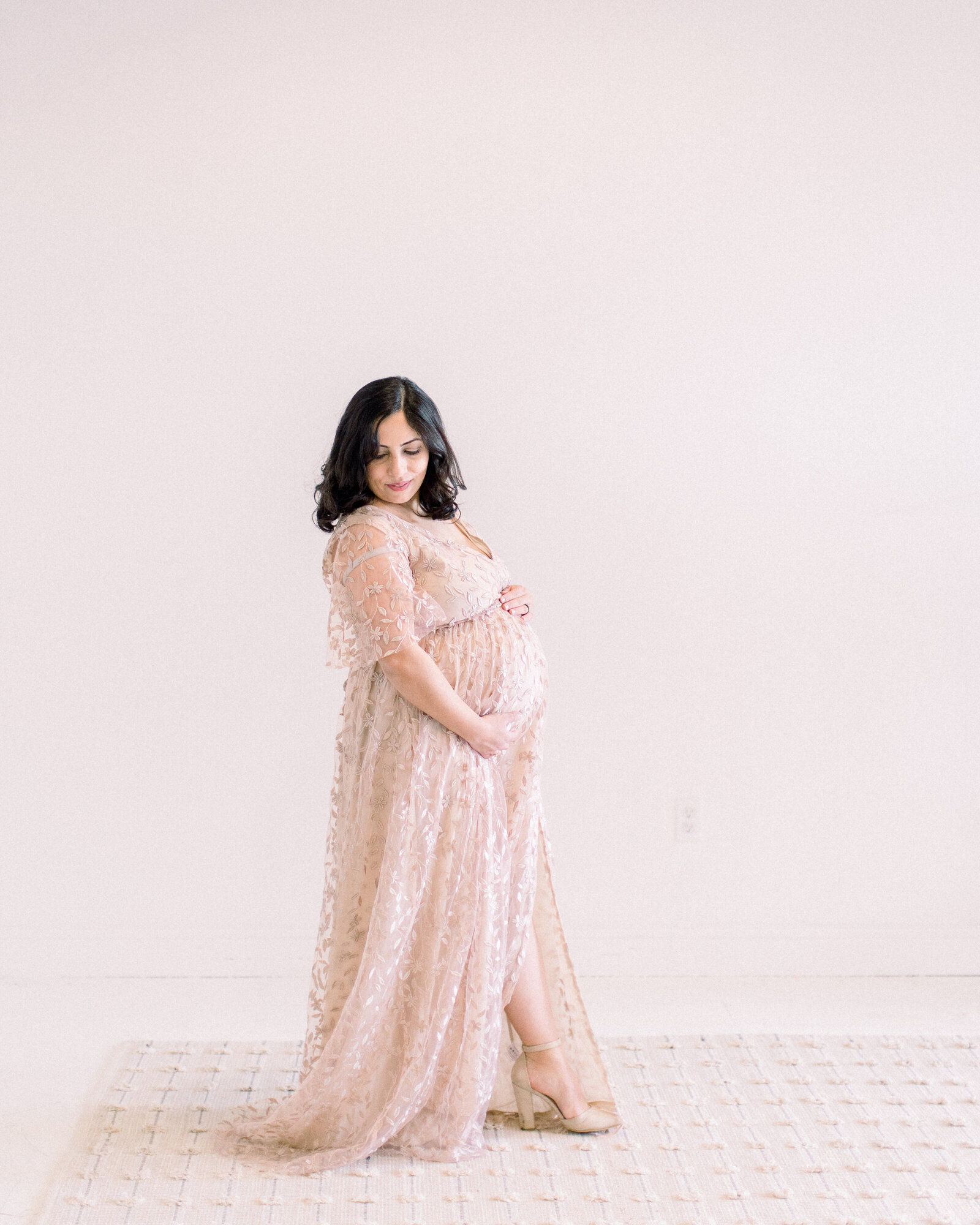 Serene portrait of pregnant mom glancing down and holding her baby bump, walking across a neutral studio by NH newborn photographer Fieldstone Studio.