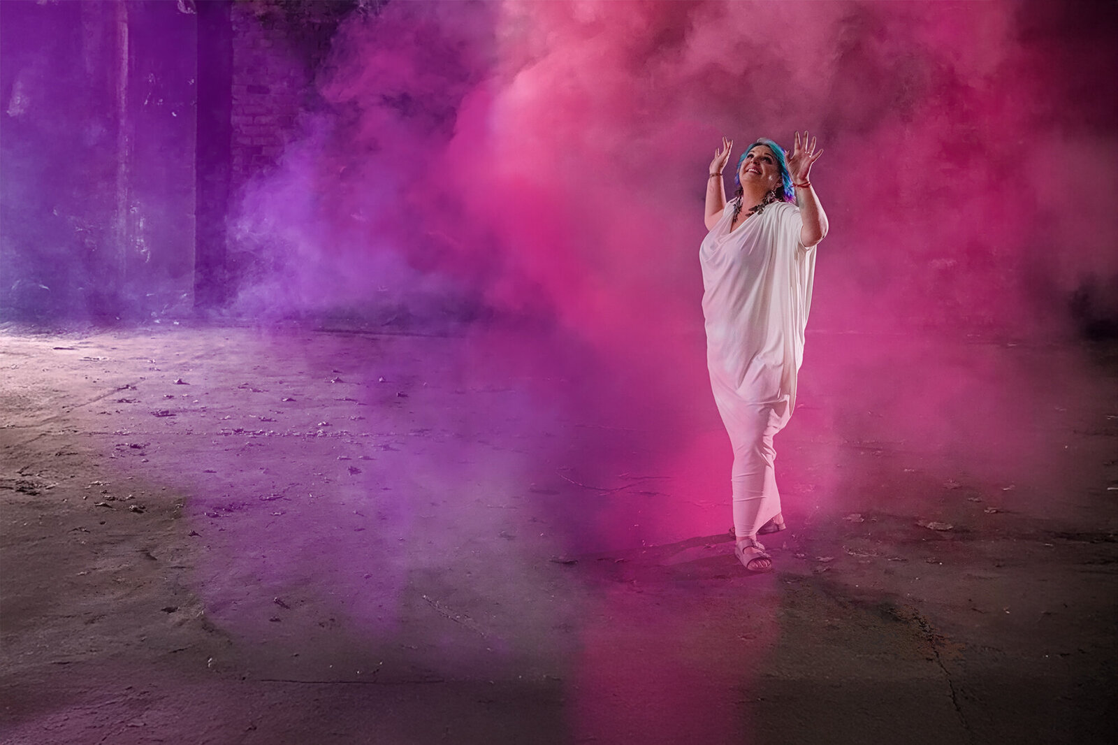 Woman in a white dress, raising her hands up, surrounded by pink and purple smoke to discover her Soul Blueprint.