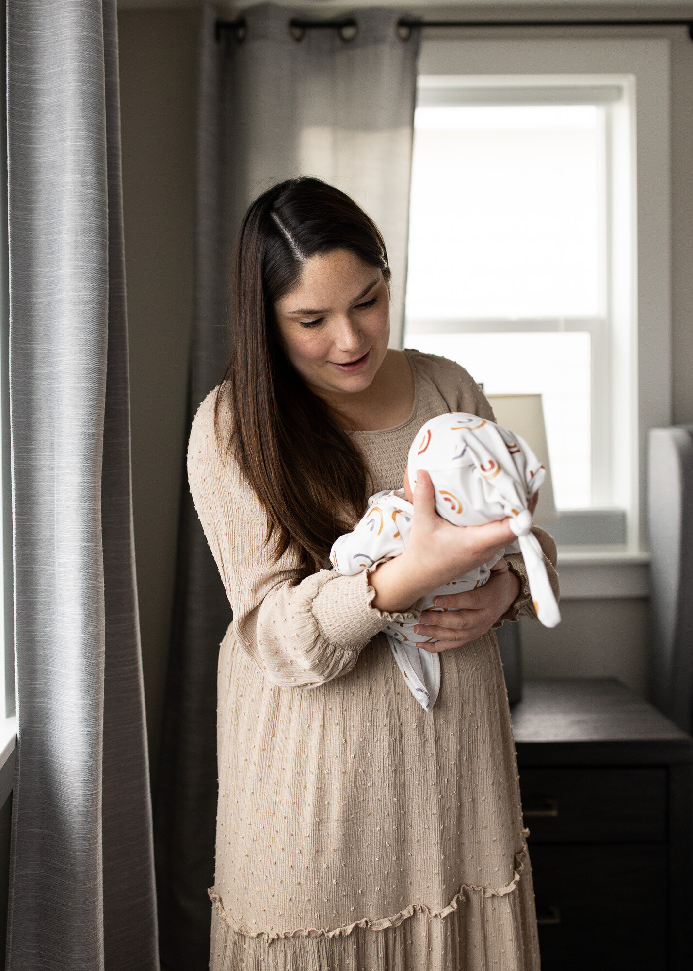 Mother gazes at newborn son by window in a session with a Portland newborn photographer.