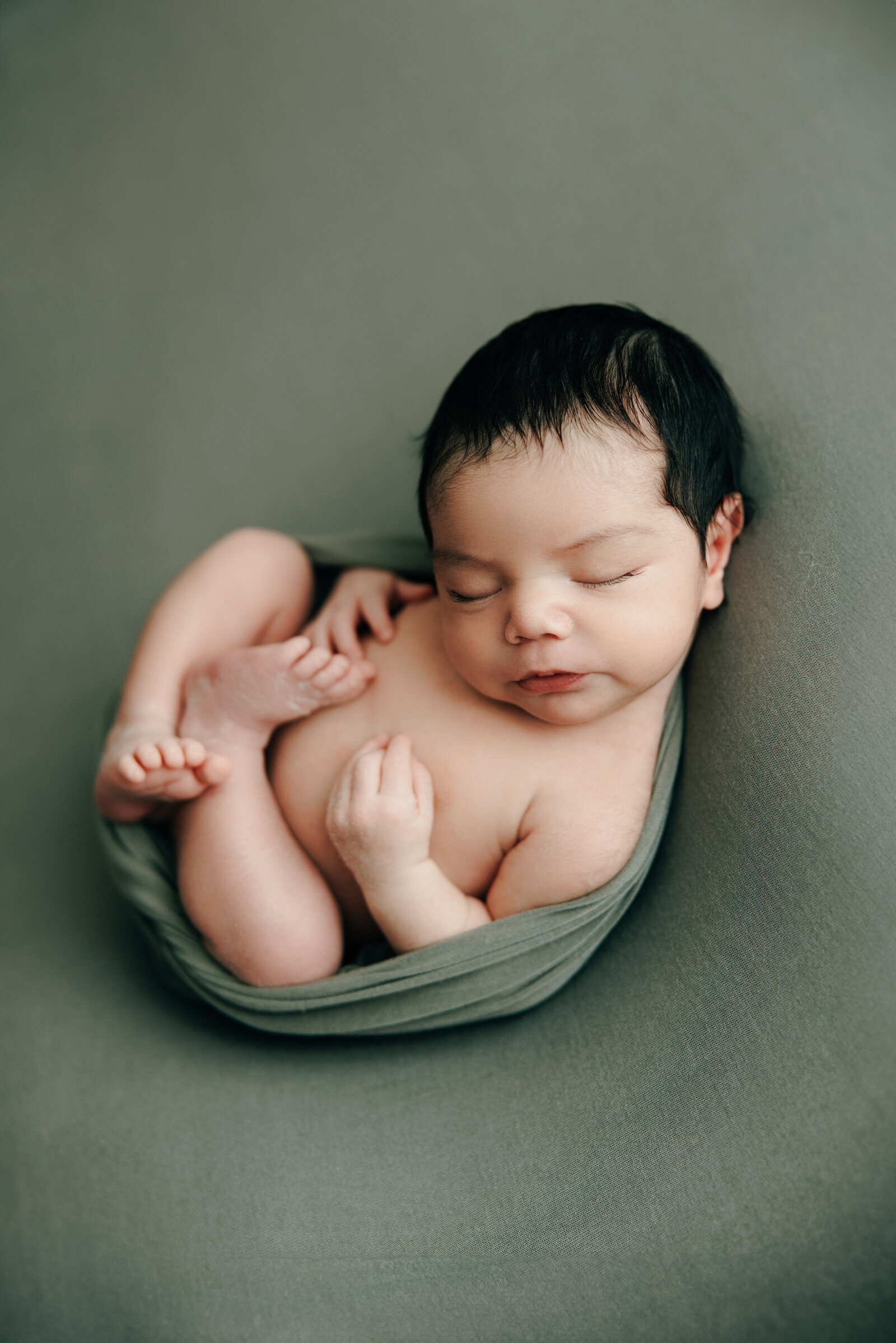 A dark haired baby poses on a green backdrop